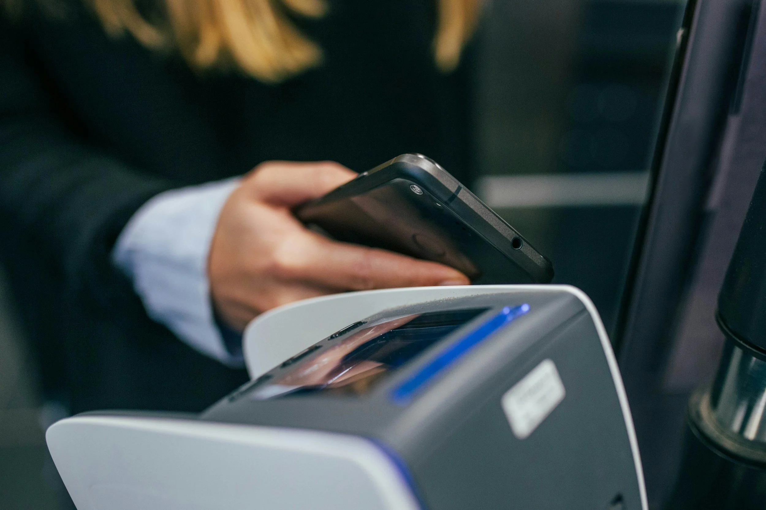 Person holding a black smartphone near a payment terminal at a checkout counter.