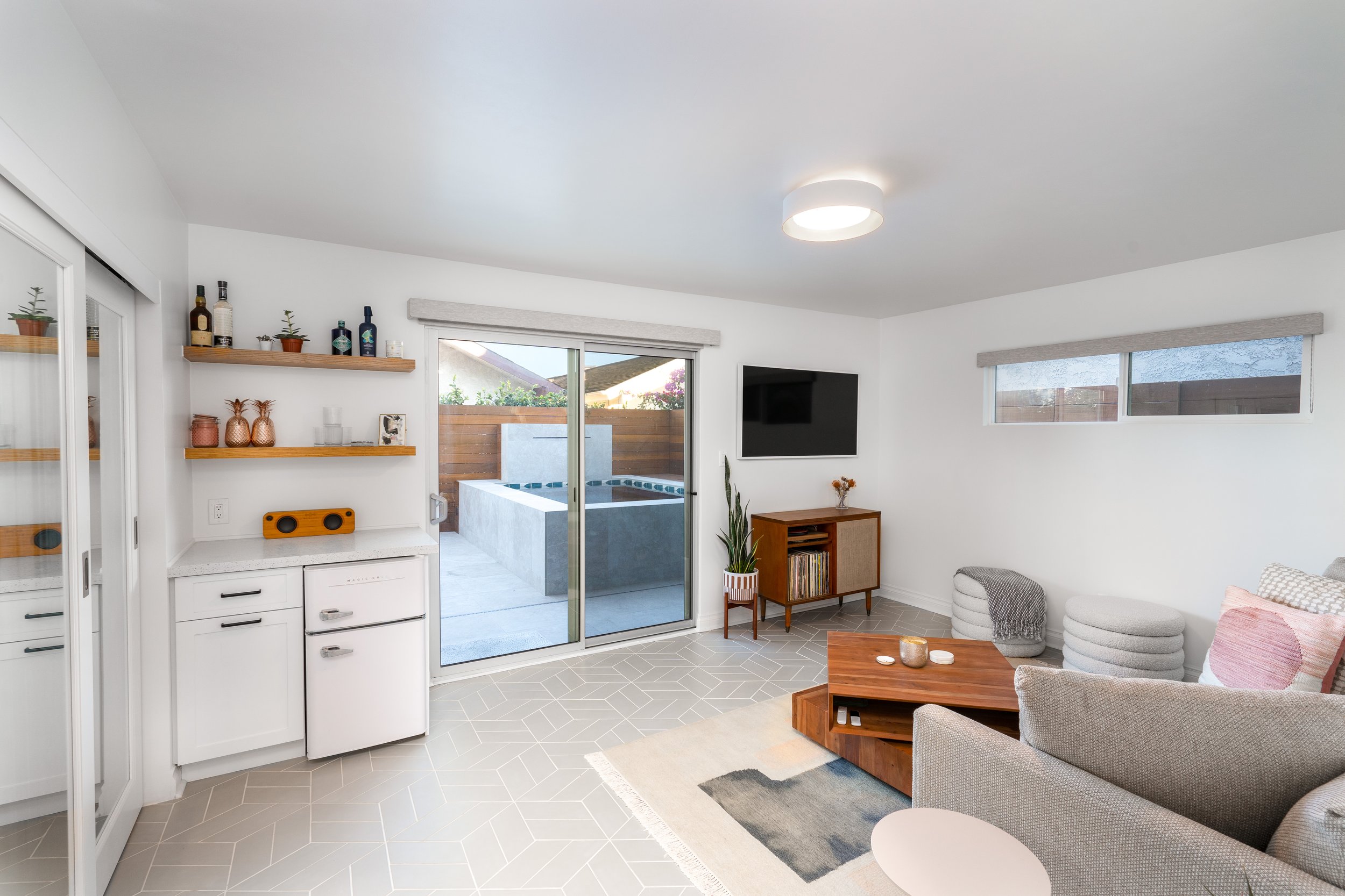 Open living space with kitchenette, sliding glass door to patio spa, modern shelving, and light tile flooring