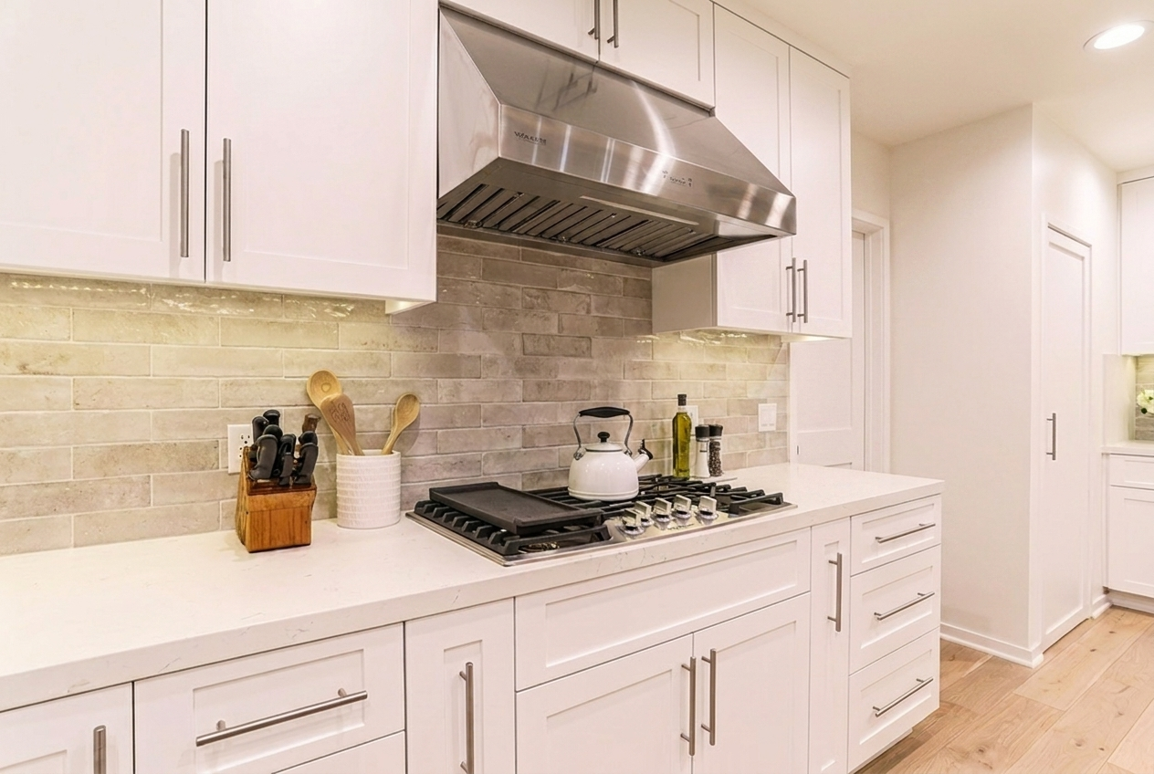 Custom modern Irvine kitchen remodel featuring stainless steel range hood, gas cooktop, white shaker cabinets, and quartz backsplash.