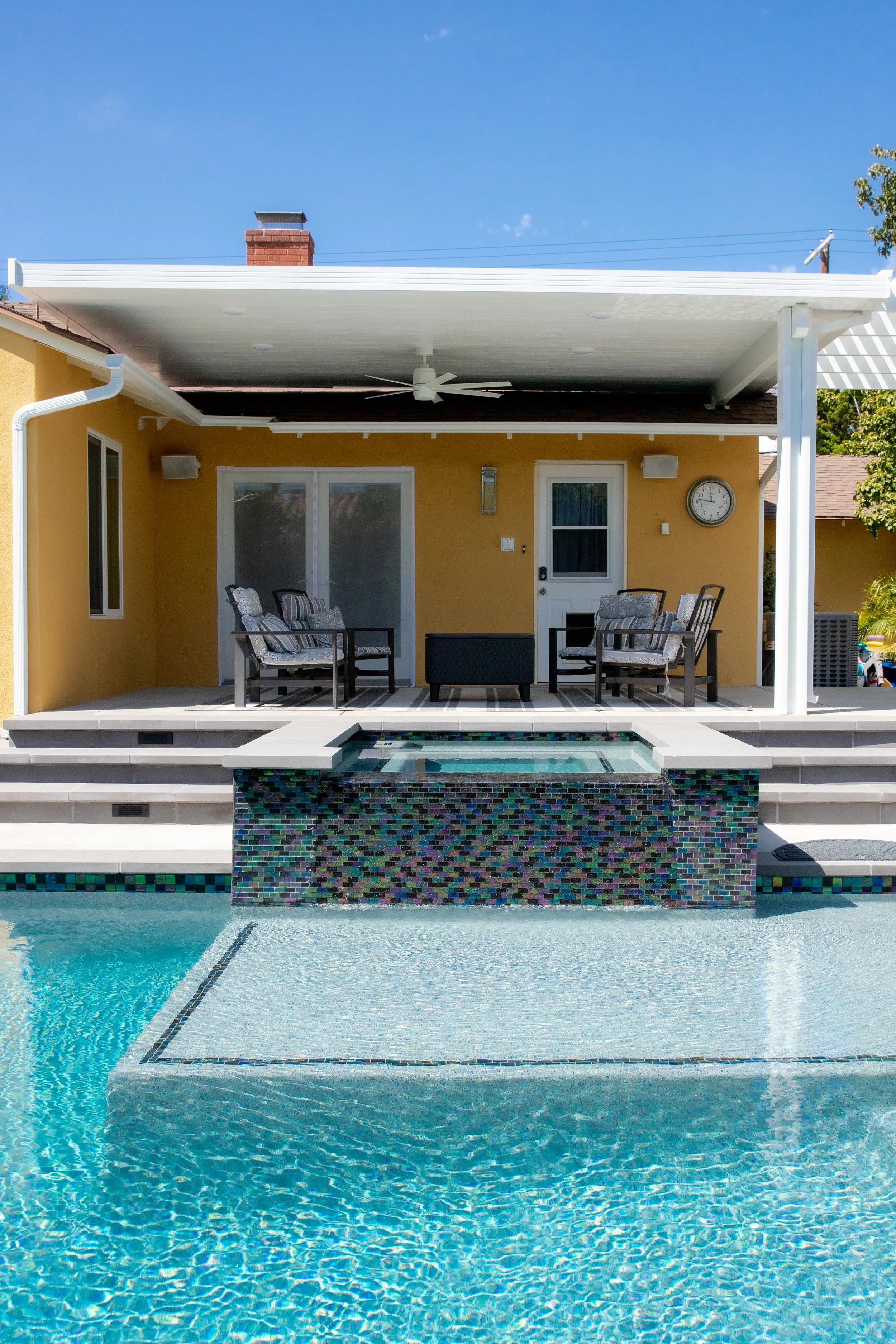 Backyard with a swimming pool, hot tub, and patio furniture under a covered porch.