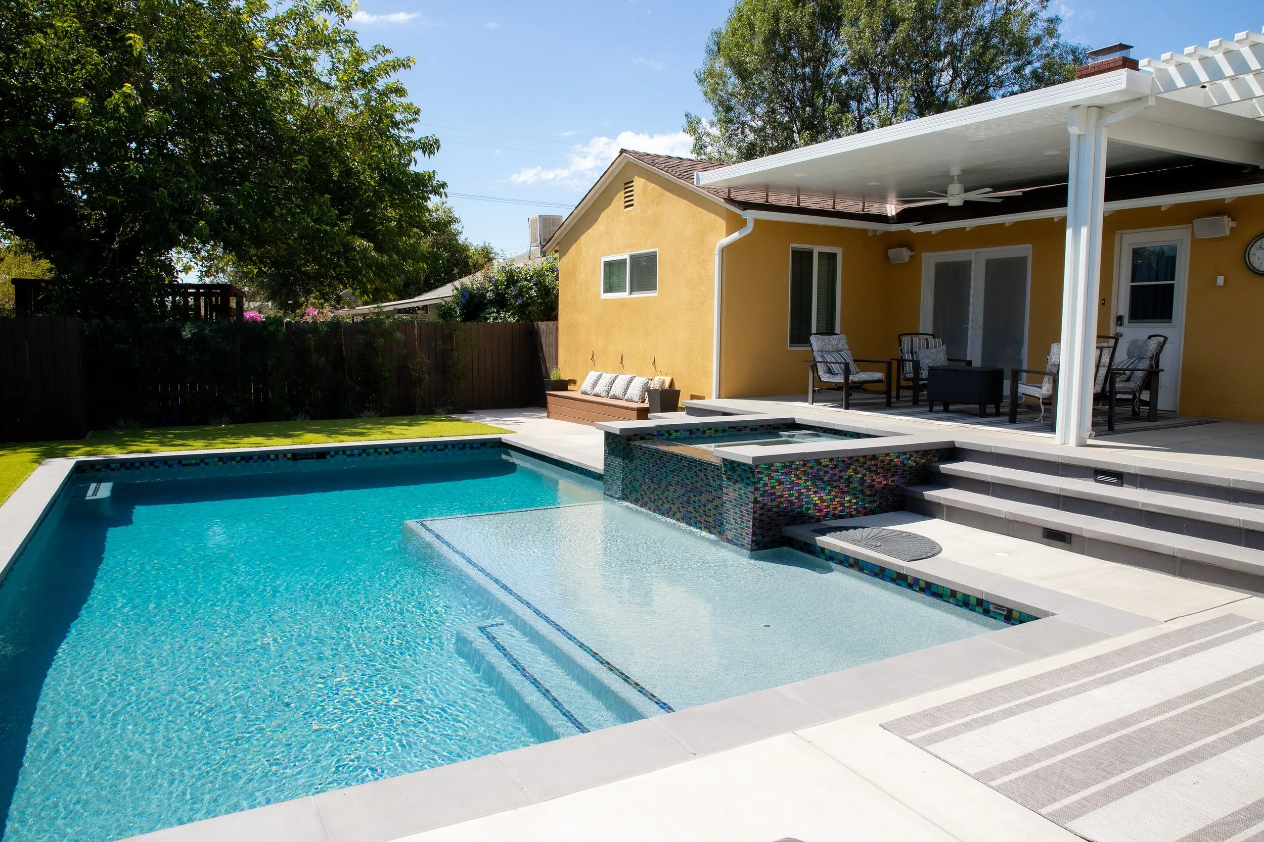 Backyard with a swimming pool, hot tub, patio furniture, and a yellow house with a covered porch.