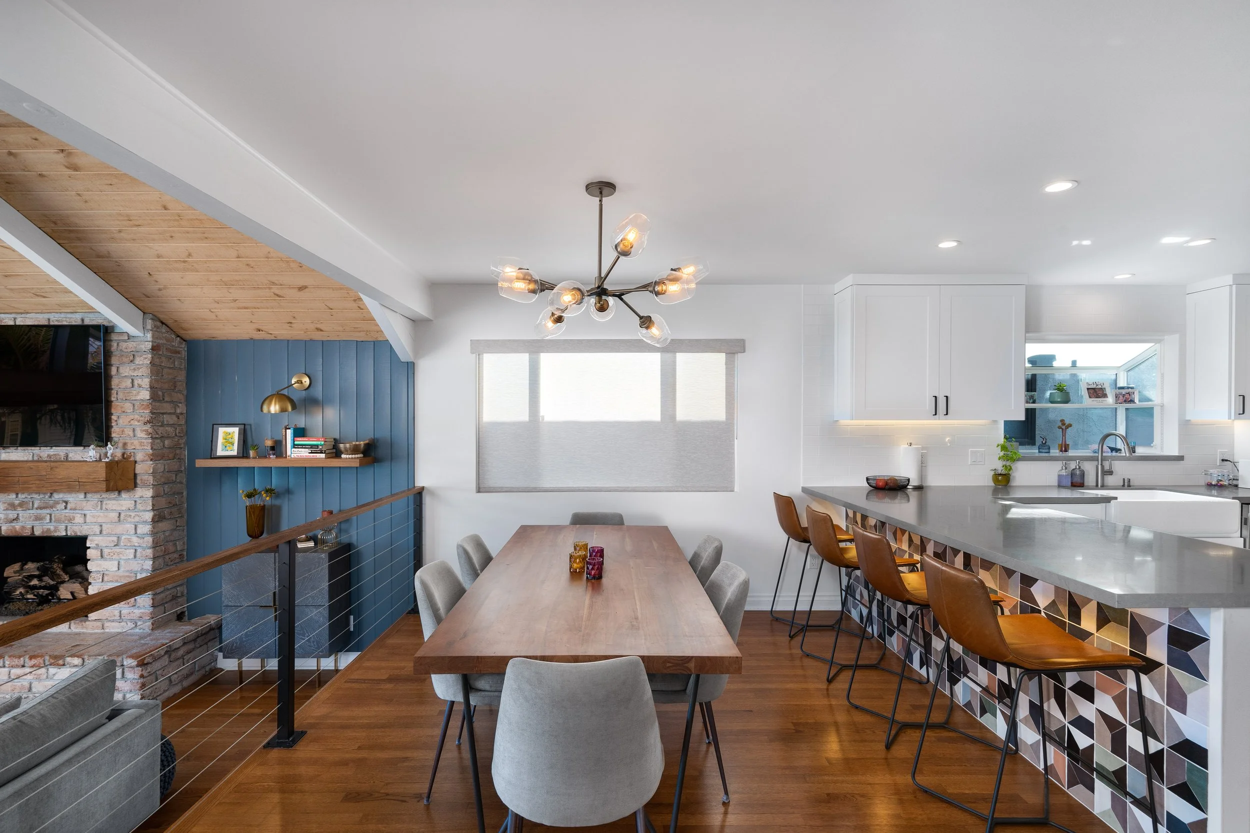 Open dining area with custom wood table, modern chandelier, kitchen island with geometric tile backsplash, white cabinetry, and bar seating in a remodeled home