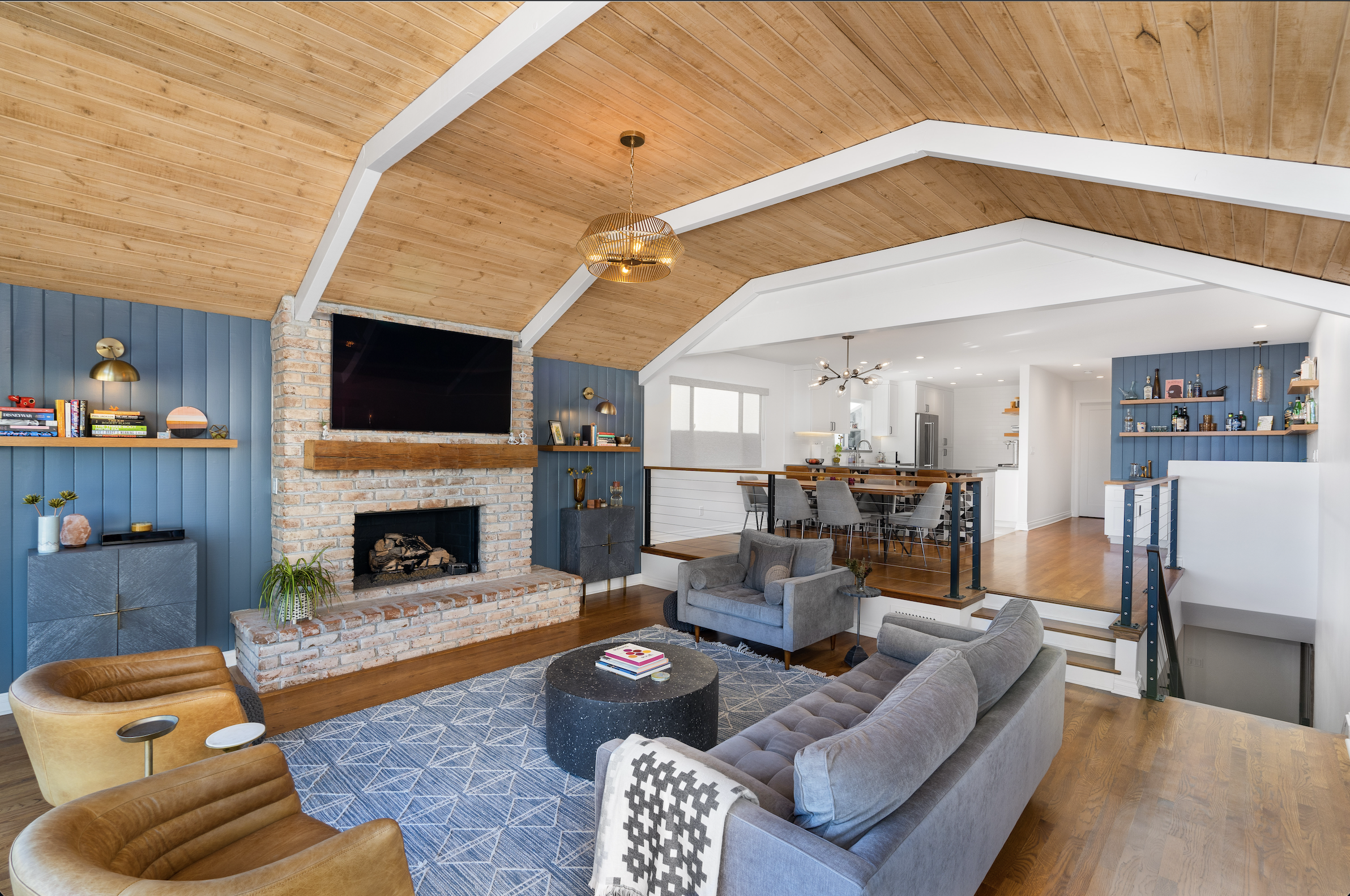 Whole-home remodeling project in Irvine featuring vaulted wood ceilings, open-concept living room, exposed brick fireplace, hardwood flooring, and modern kitchen design.