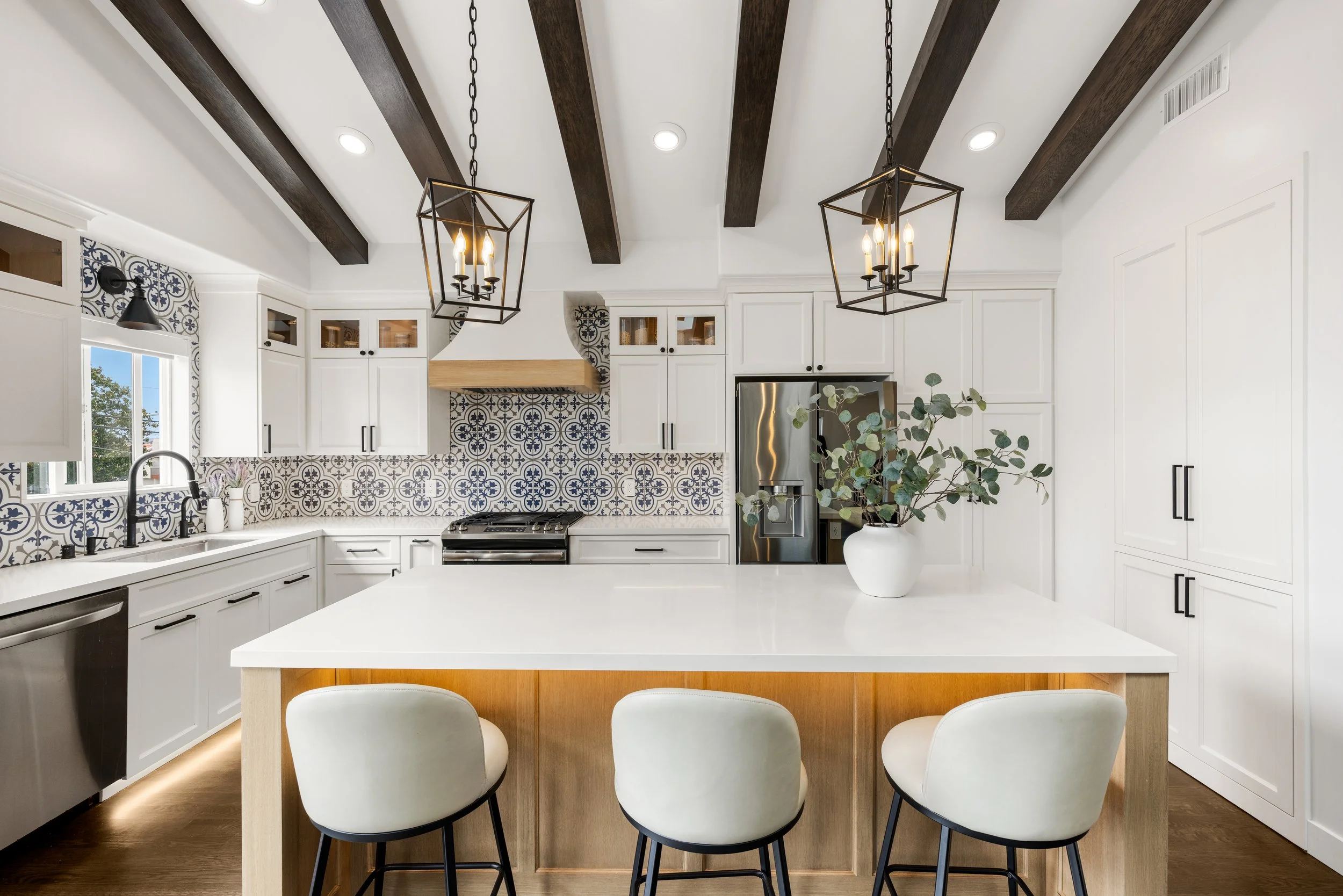 Bright Orange County kitchen remodel with white shaker cabinets, blue patterned tile backsplash, exposed wood ceiling beams, pendant lighting, and a large quartz island.