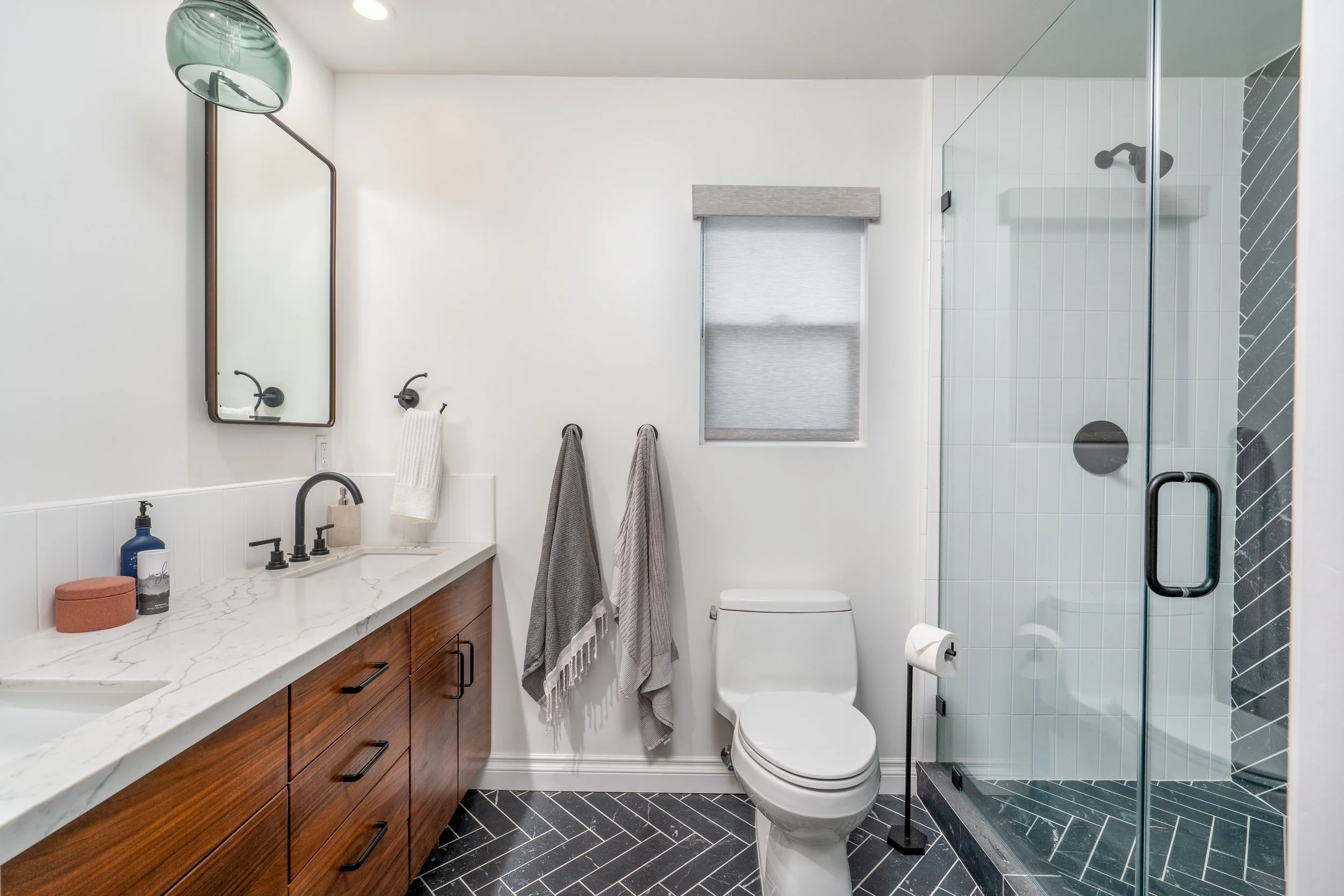 Contemporary Costa Mesa bathroom remodel with glass walk-in shower, custom vanity, black fixtures, and herringbone tile flooring