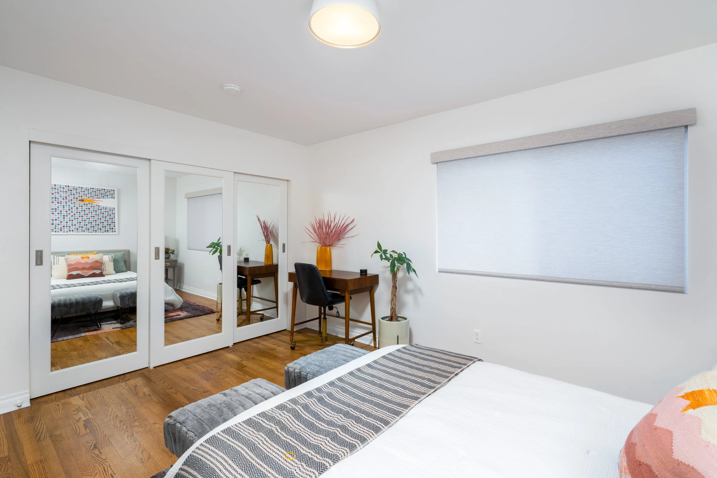 Modern bedroom with mirrored closet doors, hardwood floors, small workspace desk, and minimalist decor