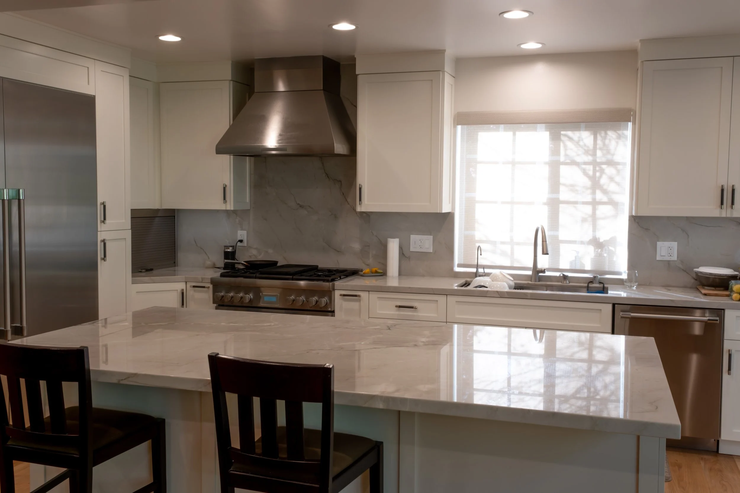 Kitchen remodel with marble countertops, custom cabinetry, stainless steel range hood and gas cooktop