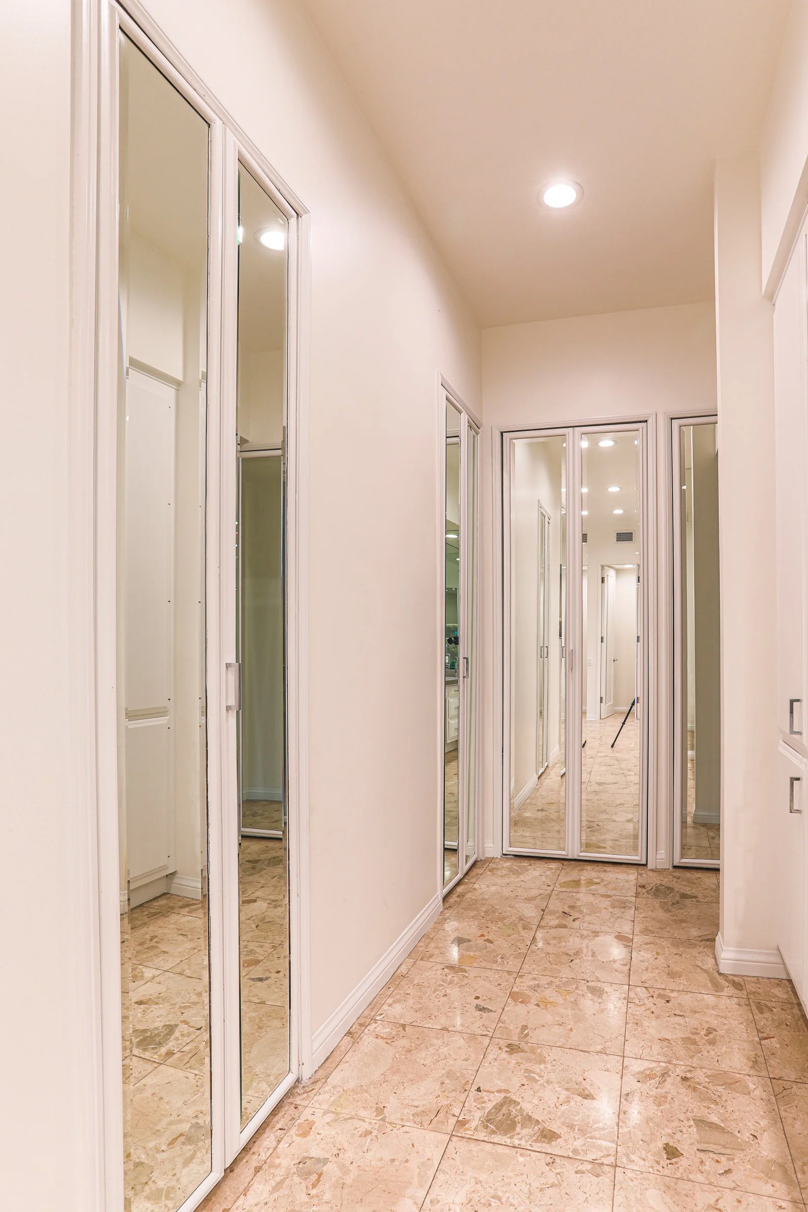 Luxury primary bathroom hallway with mirrored closet doors and marble flooring in Newport Beach home