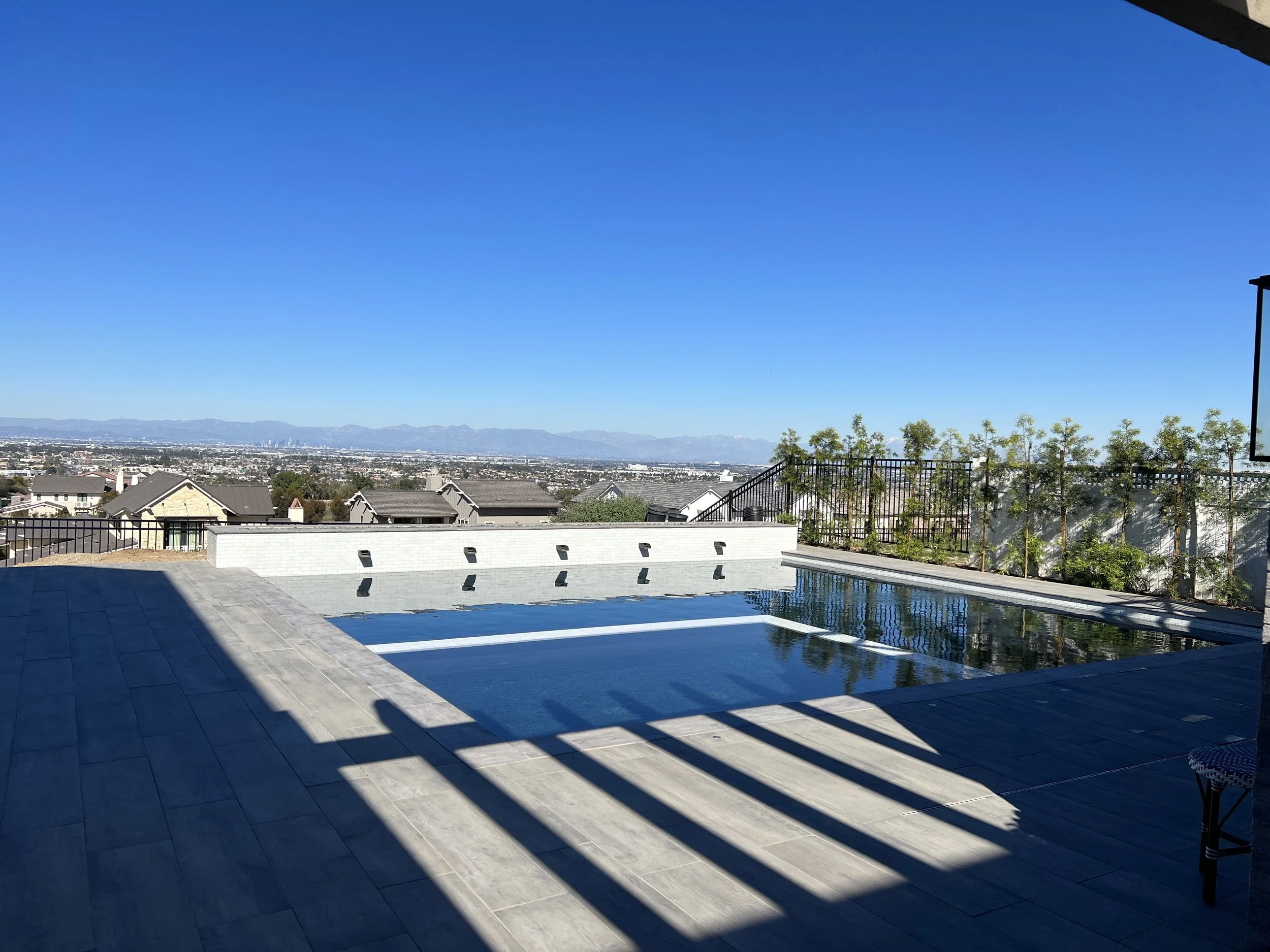 Modern infinity-edge pool with panoramic hillside views, large-format tile decking, and sleek glass railing for a luxury outdoor living space.
