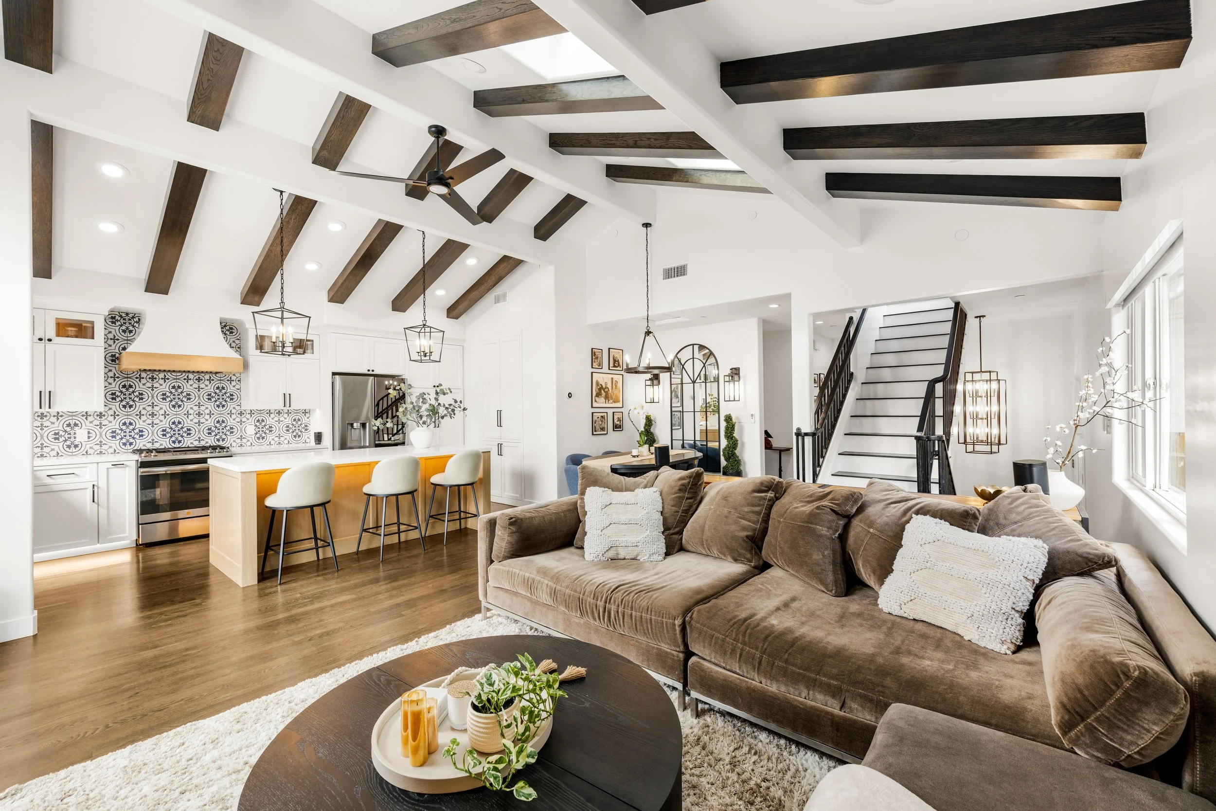 Open-concept Orange County home remodel with a white kitchen, patterned tile backsplash, wood ceiling beams, large island, and adjoining living room.