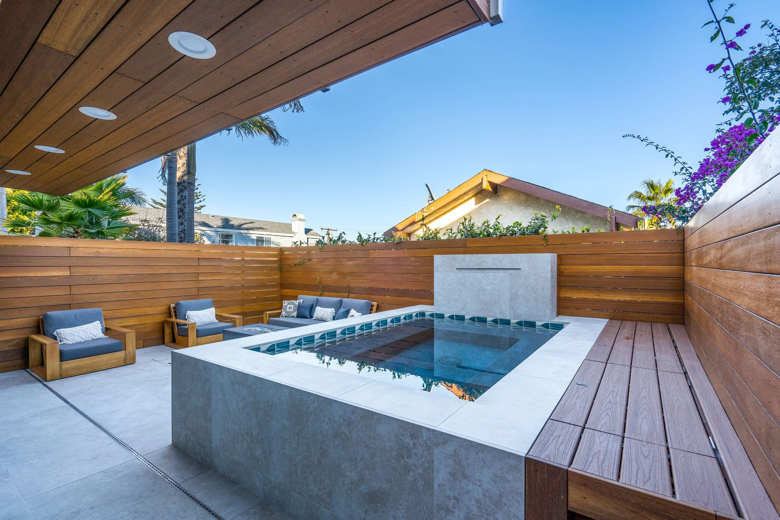 Modern plunge pool and spa with clean concrete finish, wood privacy fencing, built-in seating, and minimalist outdoor design.