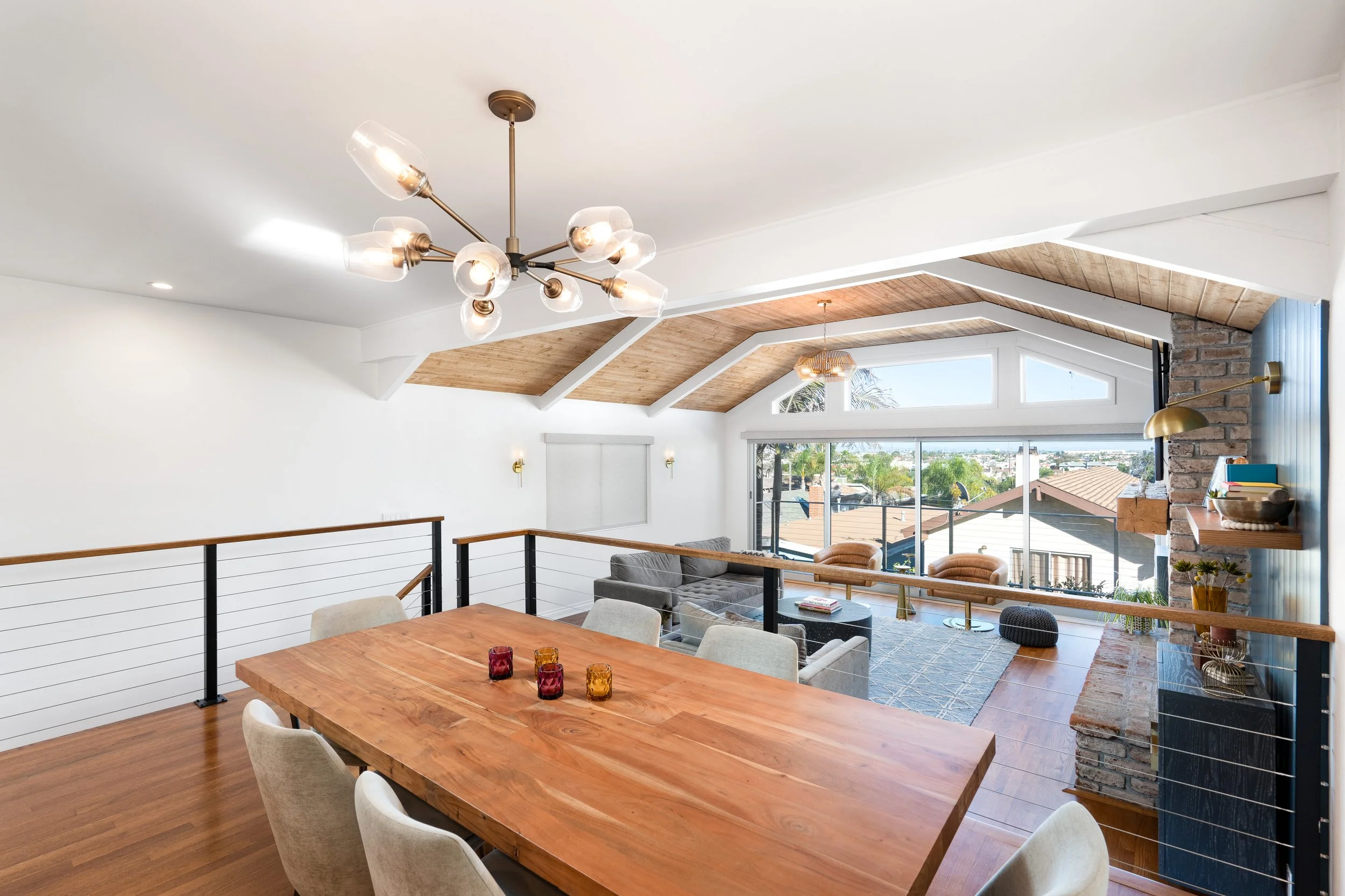 Warm modern dining room with wood table, designer chandelier, vaulted ceilings, and open-concept kitchen connection.