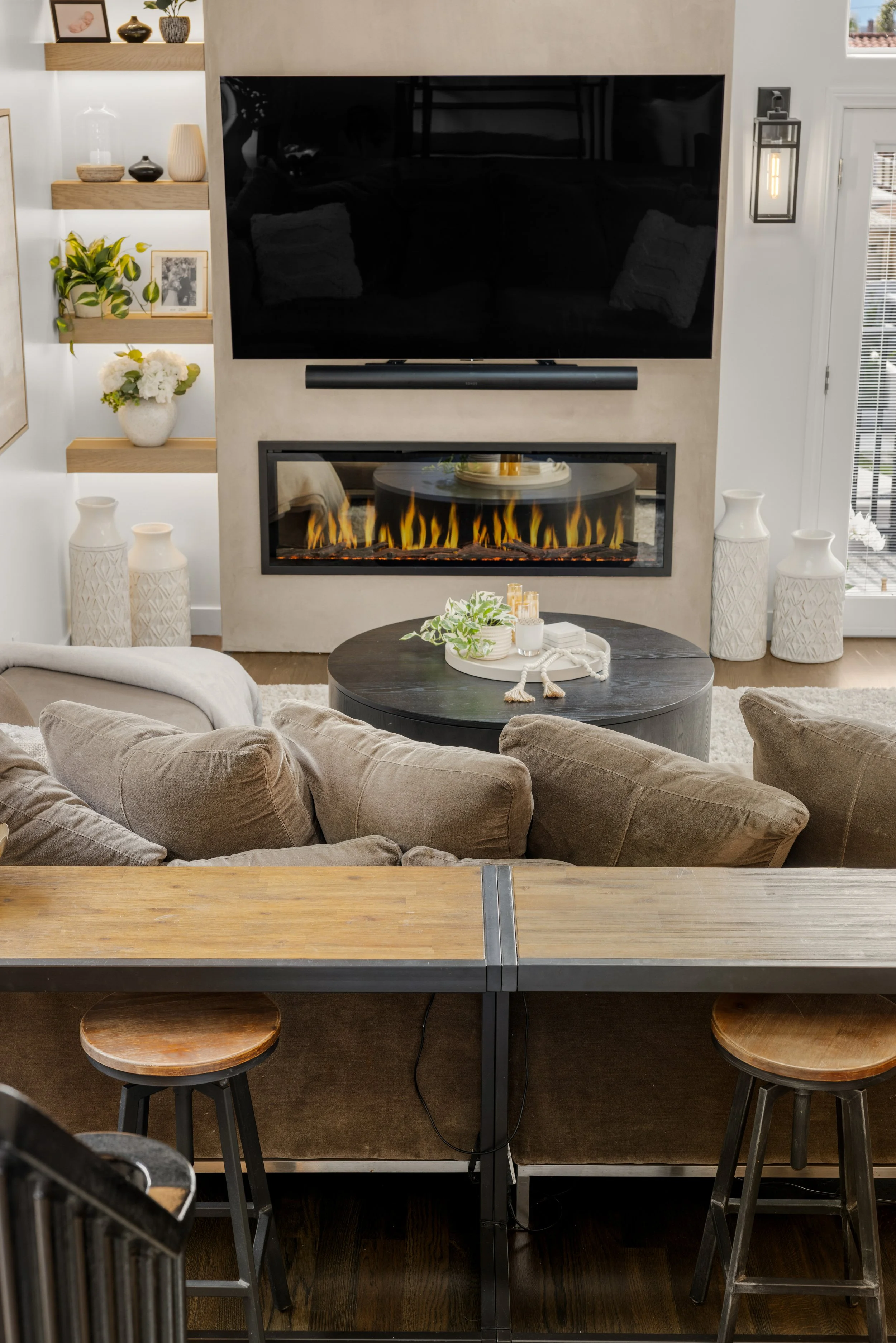 Open-concept living room and kitchen with a wall-mounted TV, modern linear fireplace, built-in shelving, and a wood breakfast bar with stools.