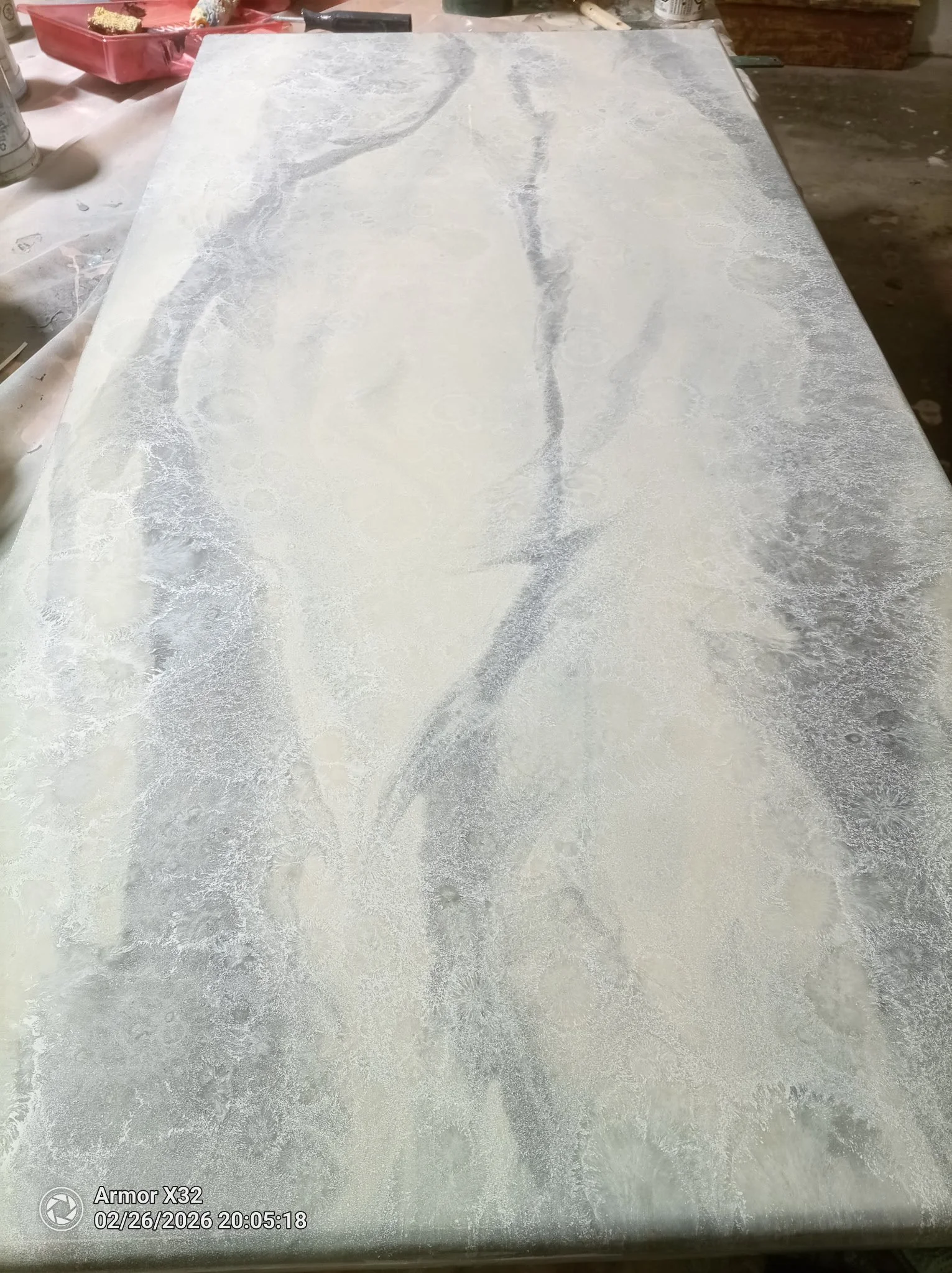 A marble or quartz countertop with white and gray veining. There are some containers and tools around it, indicating a work area, possibly for fabrication or installation.
