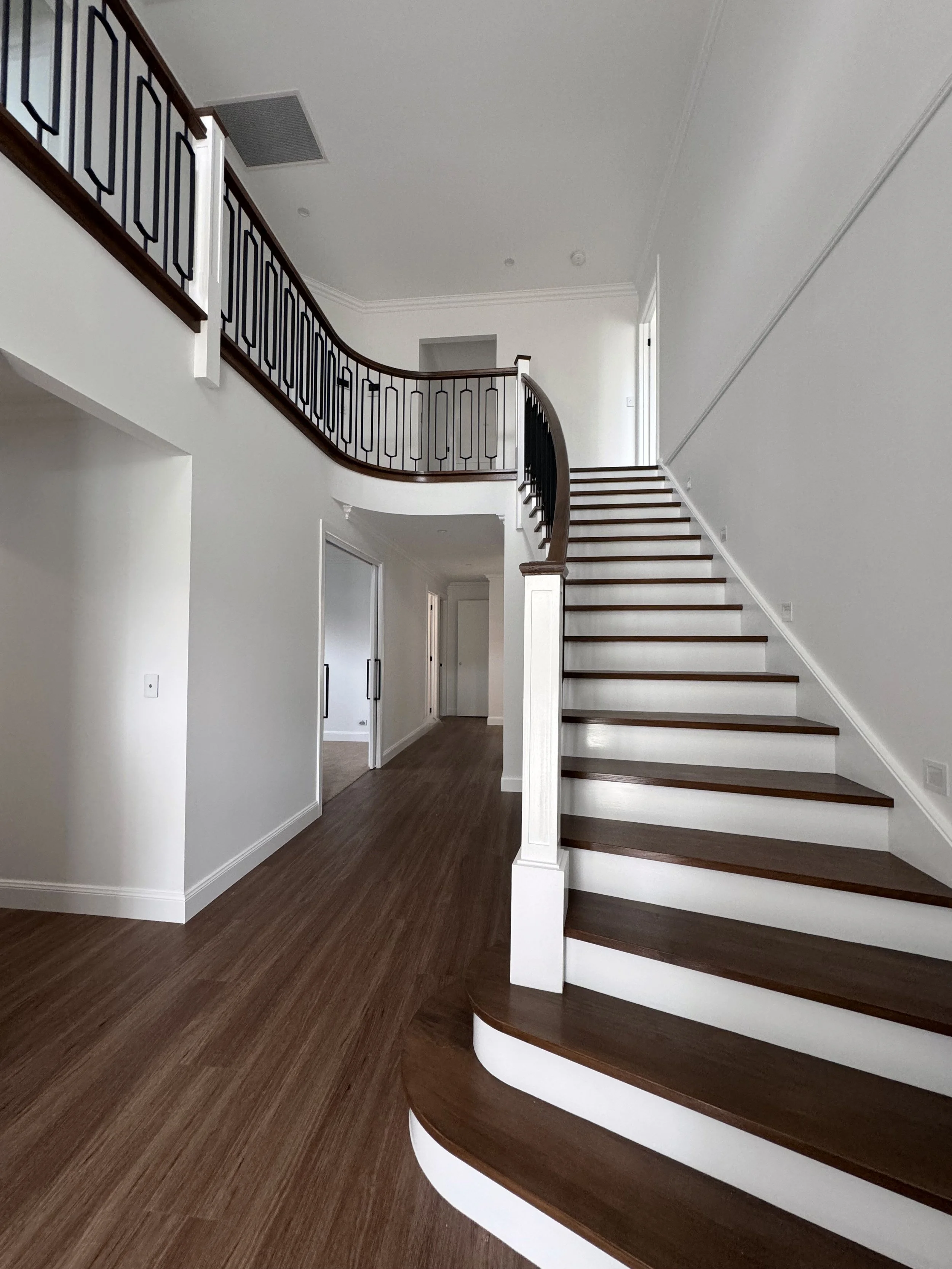 Interior view of a house with a wooden staircase leading to an upper floor, white walls, wood flooring, and a curved railing.
