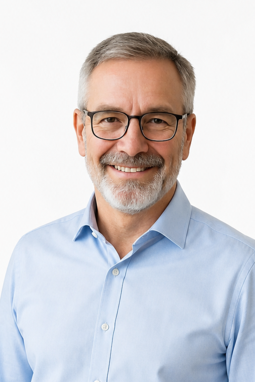 A smiling middle-aged man with gray hair and beard, wearing glasses and a light blue button-up shirt, against a white background.