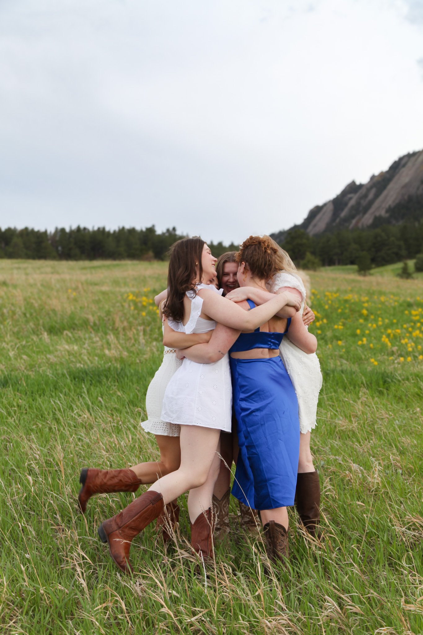 Group of women hugging in a grassy field with mountains in the background.