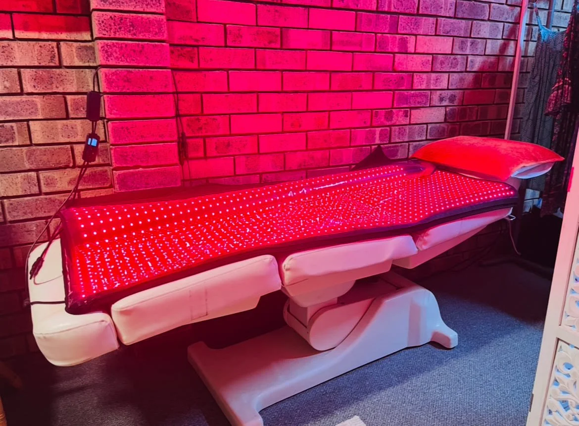 A workspace with a massage table covered in a red LED light strip, a pillow at one end, against a brick wall, with electrical cords nearby.