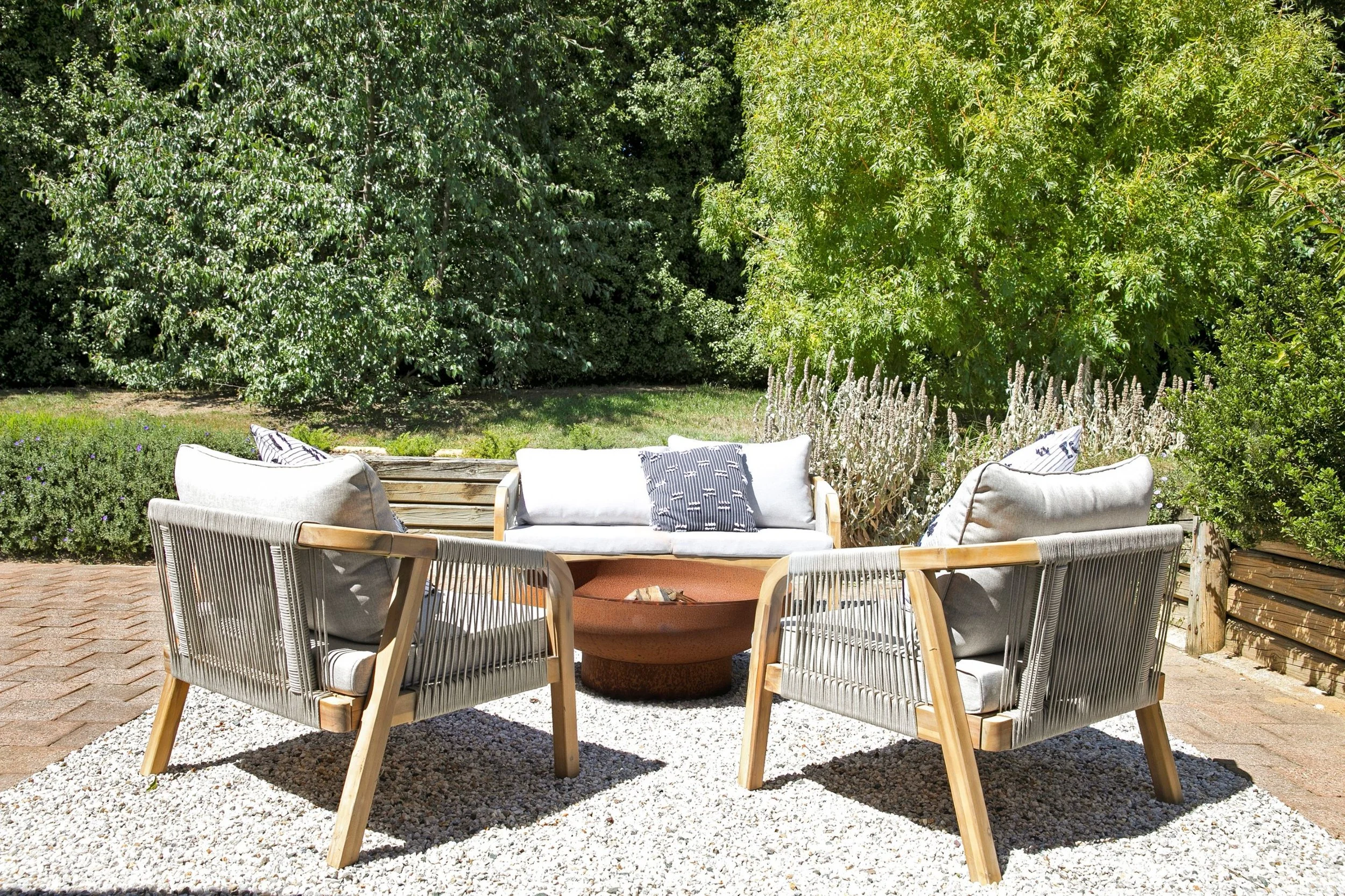 An inviting patio by Oak & Olive Homes with a lounge and two armchairs surrounding a fire pit, creating a warm atmosphere for outdoor enjoyment