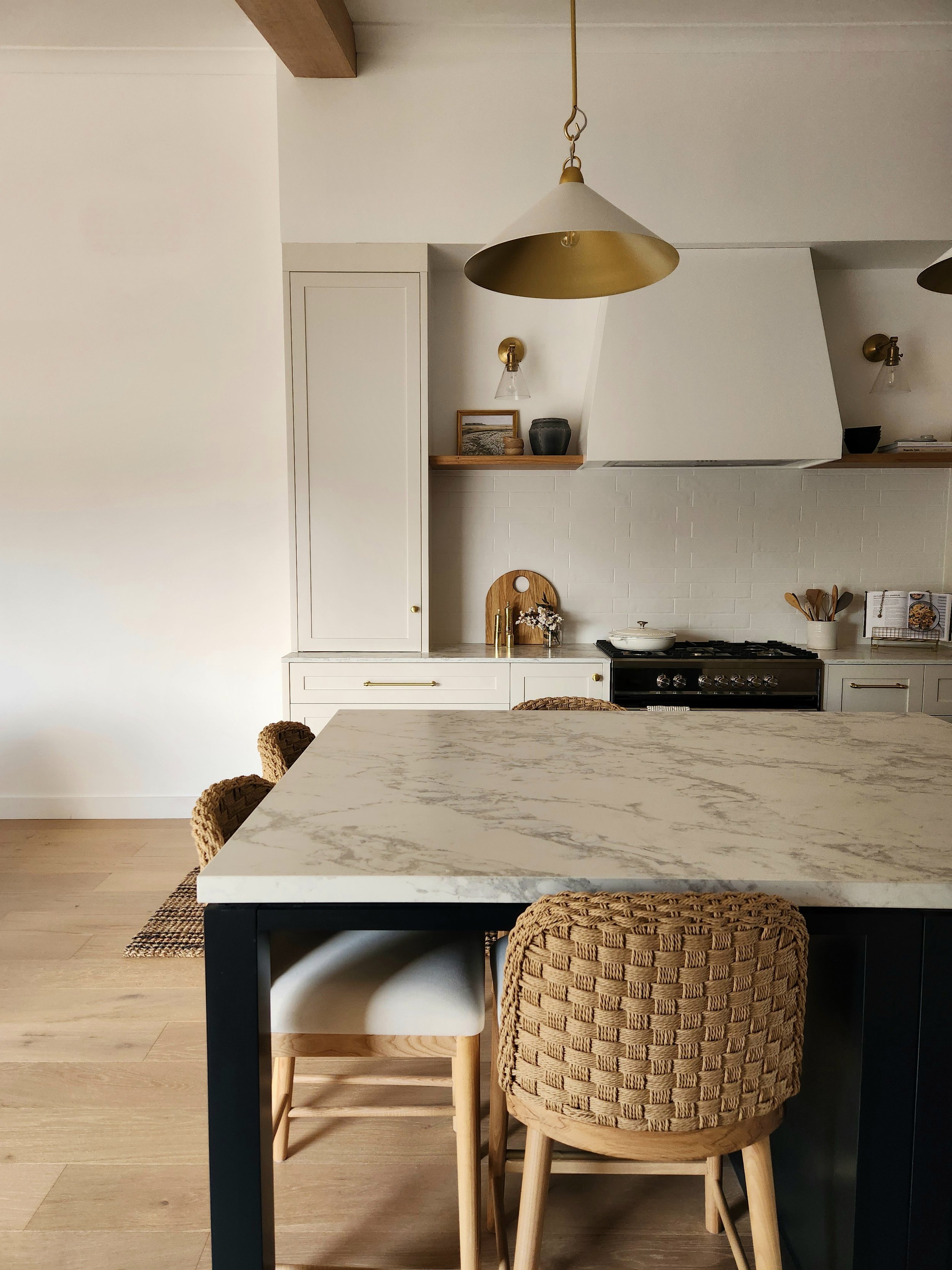 A modern kitchen featuring elegant marble countertops, designer brass pendant lights and two-tone cabinets.