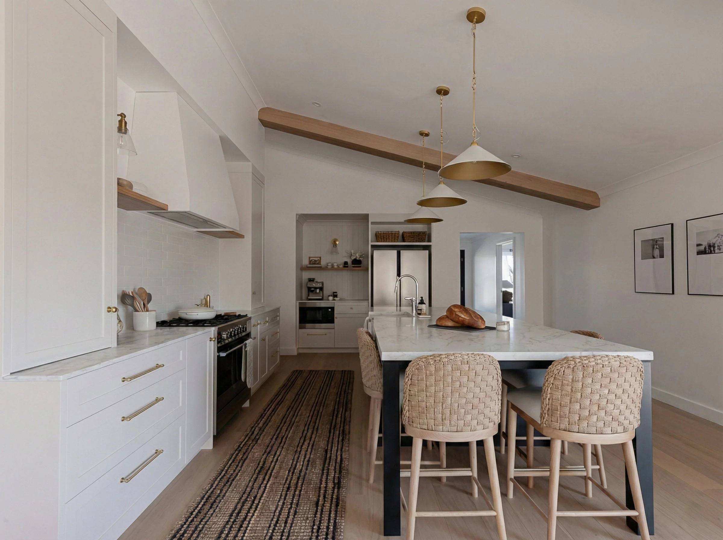 Modern organic kitchen by Oak & Olive Homes with white shaker cabinets, marble island, woven bar stools, oak wood beams & brass pendant lighting