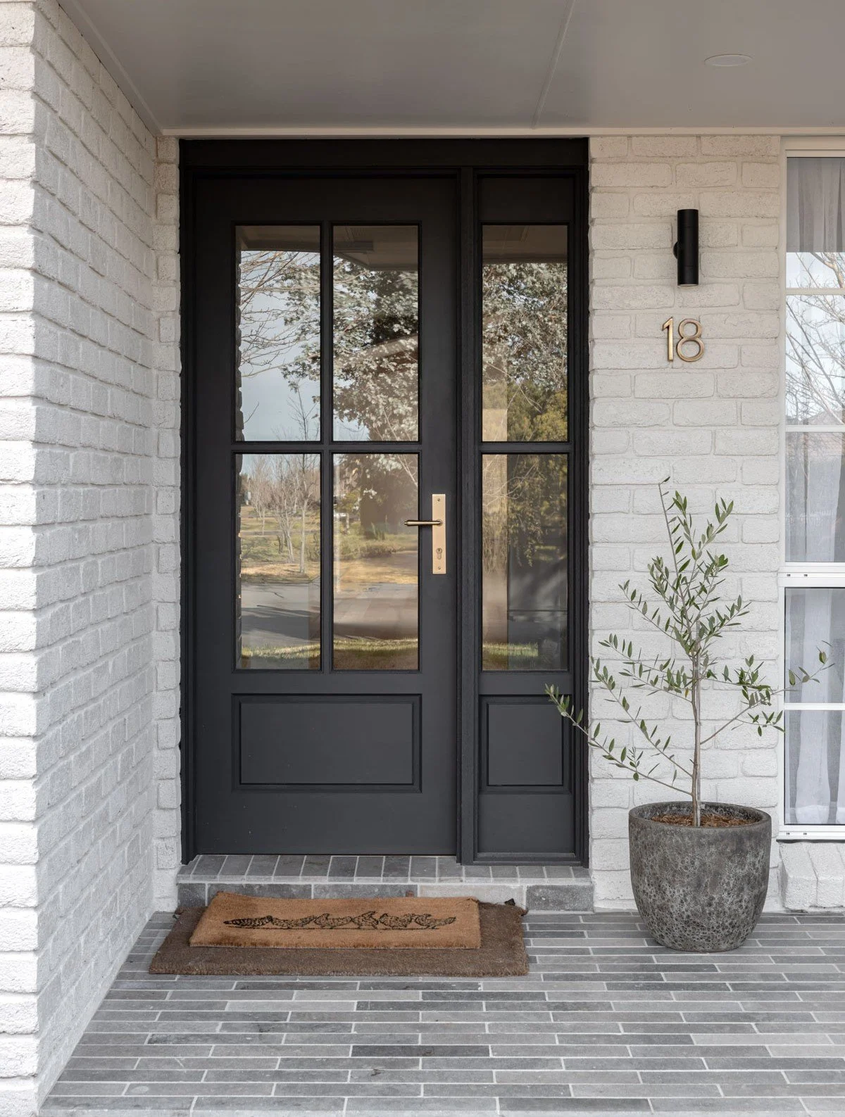 Country home front door porch by Oak & Olive Homes with charcoal glass French Door, Limestone floor tiles and a potted Olive Tree