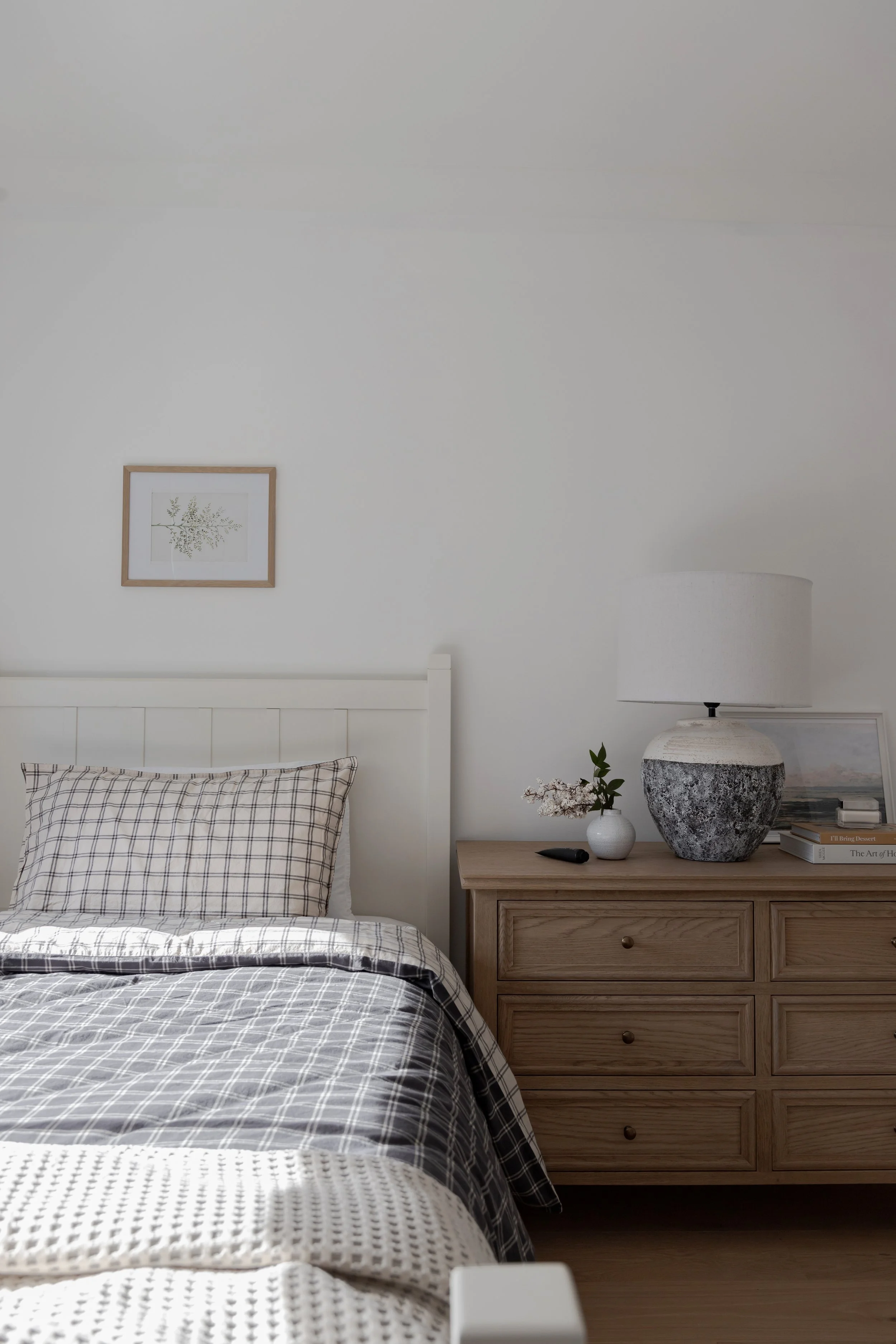 A cozy kids bedroom by Oak & Olive Homes featuring a neatly made bed, wooden dresser, and a pottery lamp