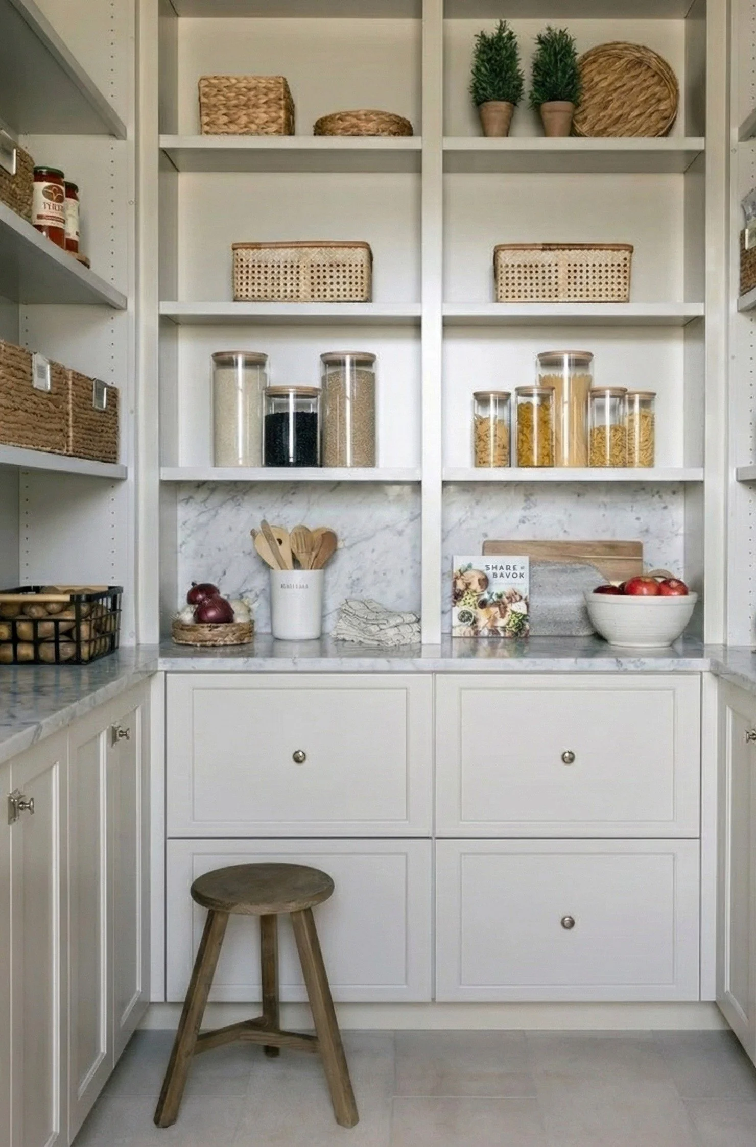 A bright walk-in pantry featuring marble countertops and white open shelving filled with woven baskets and glass jars