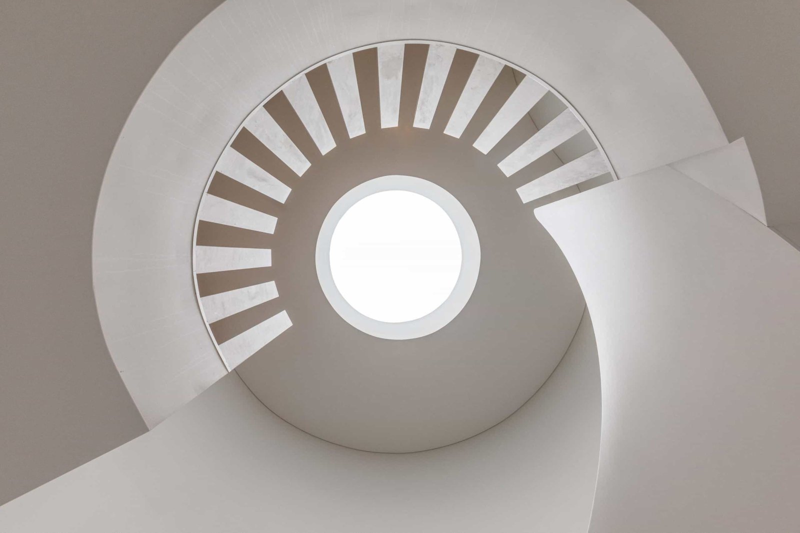 Looking up through a spiral staircase to a large round skylight