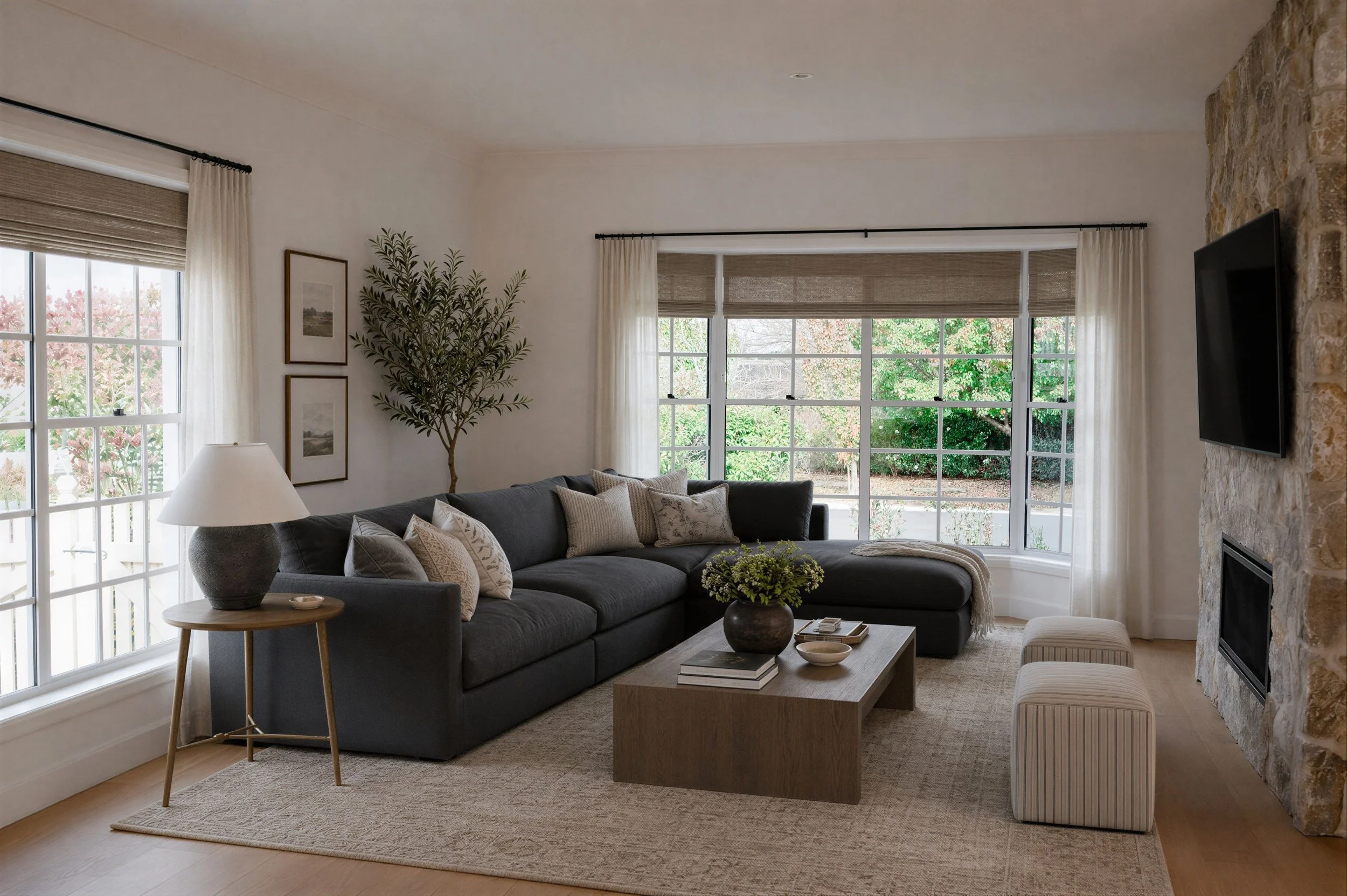 Oak & Olive Homes interior design featuring a cozy living room with a stone fireplace, dark sectional sofa, linen curtains, wood furniture and layered textures. Warm organic styling and a timeless neutral palette to create an inviting living space