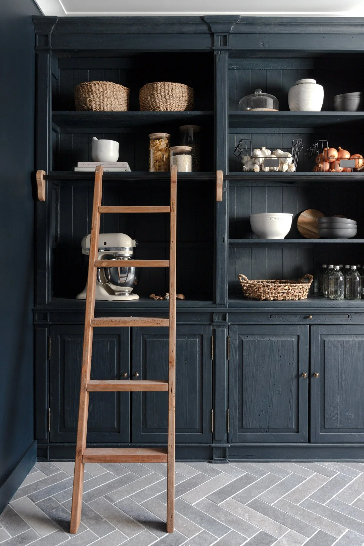 Built-in pantry by Oak & Olive Homes showcasing deep blue cabinets and a wooden ladder for reaching high storage areas.