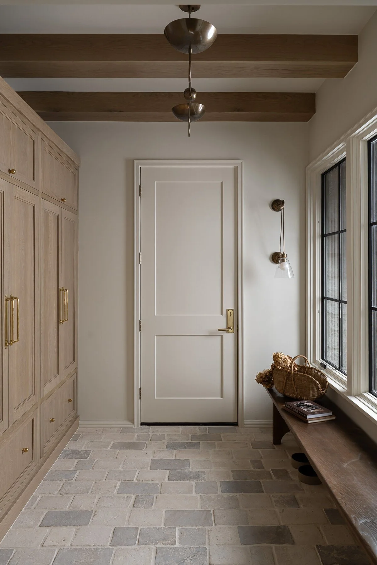 warm mudroom with wood ceiling beams, tumbled stone tiles and wood mud cabinetry