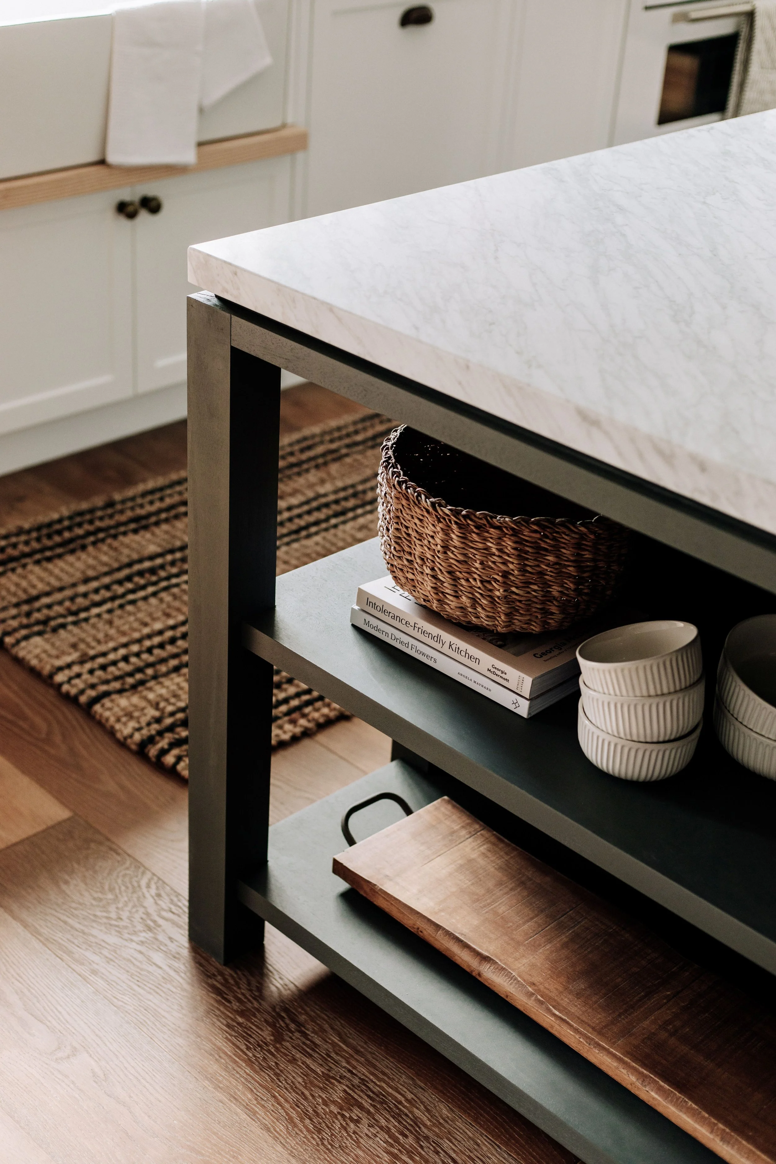 A dark kitchen island by Oak & Olive Homes featuring a sleek Carrara marble top and section of open shelves for storage and display