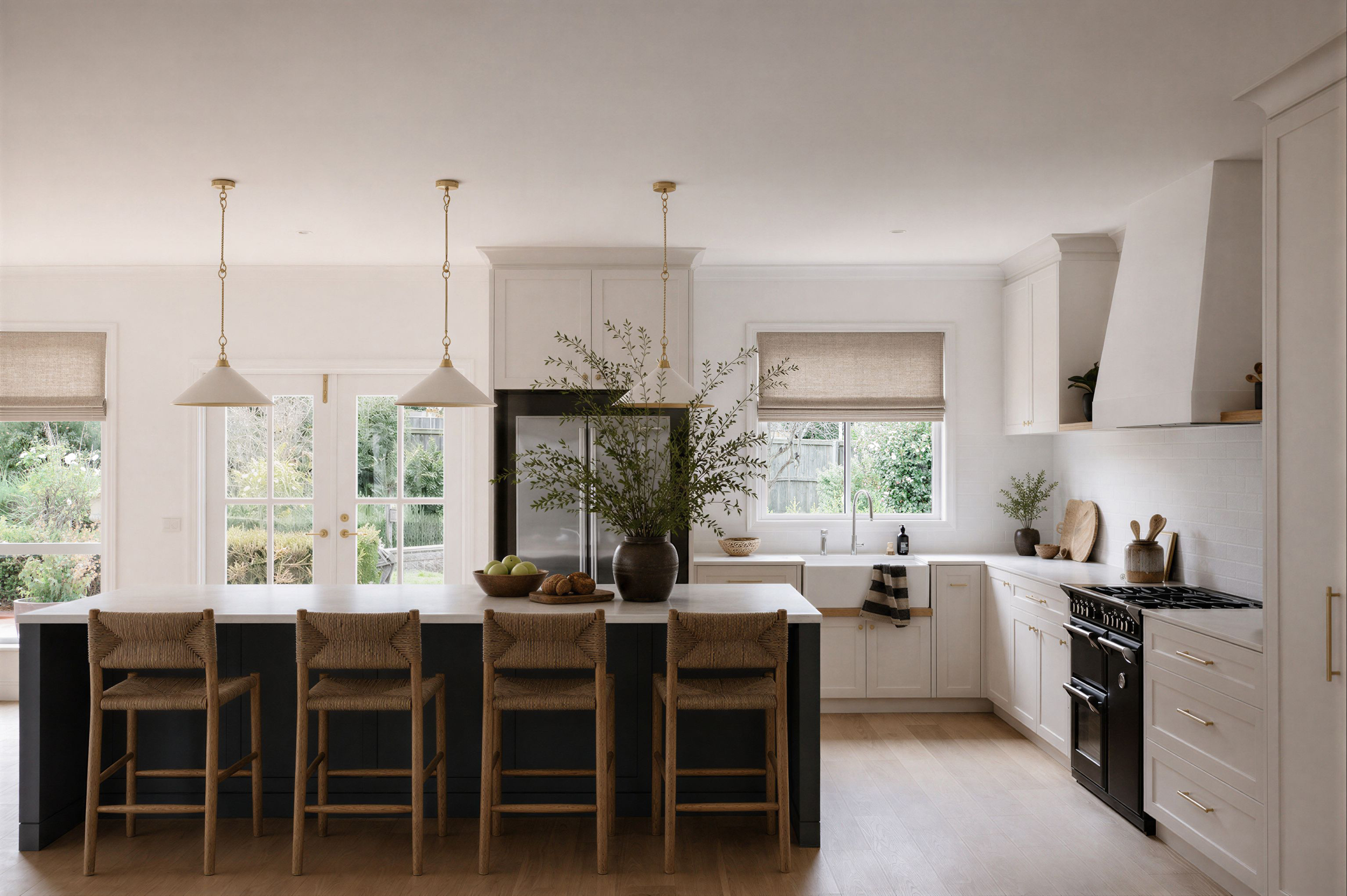 Oak & Olive Homes interior design showcasing a bright modern farmhouse kitchen with white cabinetry, brass pendant lighting, dark island, woven counter stools, natural wood floors, and organic greenery. Elegant neutral kitchen renovation with timeles