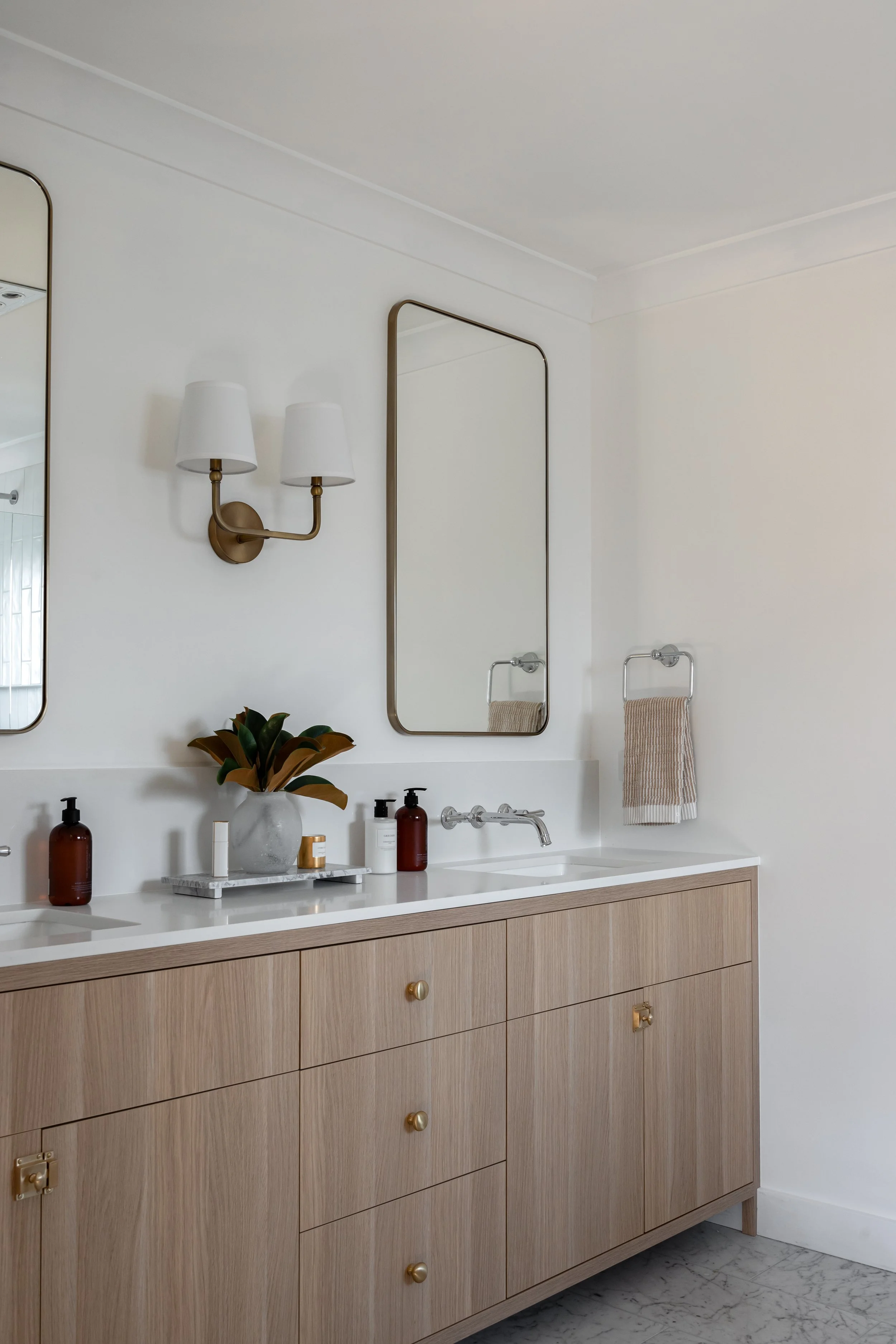 A modern bathroom by Oak & Olive Homes featuring two sinks, brass dual arm wall light & large brass mirrors 