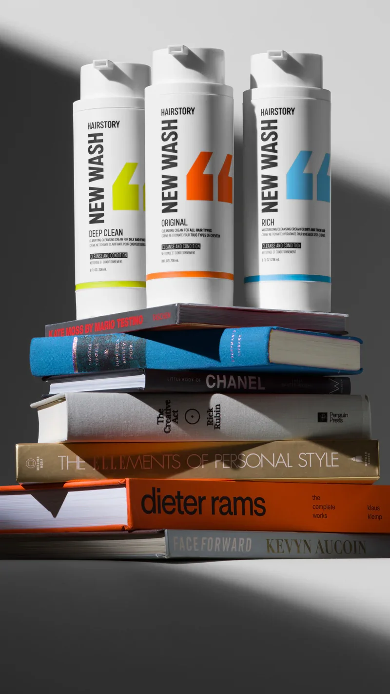 Stack of books with three hair care products on top, including 'New Wash' bottles in different variants.