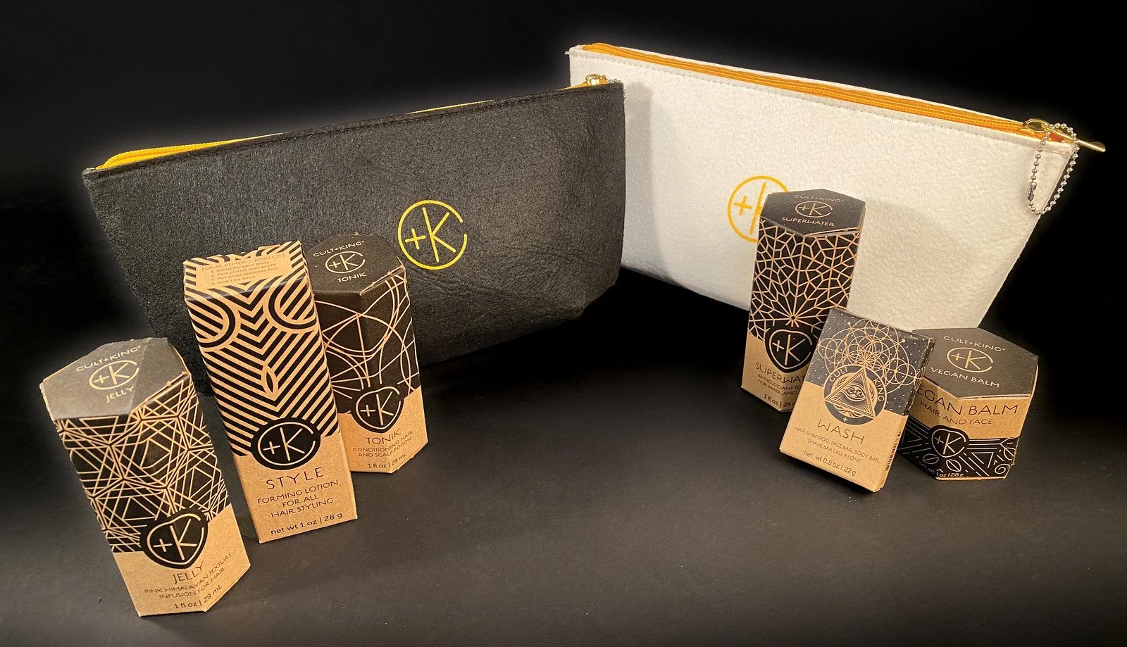 Two black and white zippered pouches with a yellow logo, surrounded by six small boxes of skincare or cosmetic products with black and rose gold designs, on a black surface. Cult+King salon retailer Ballard, Seattle