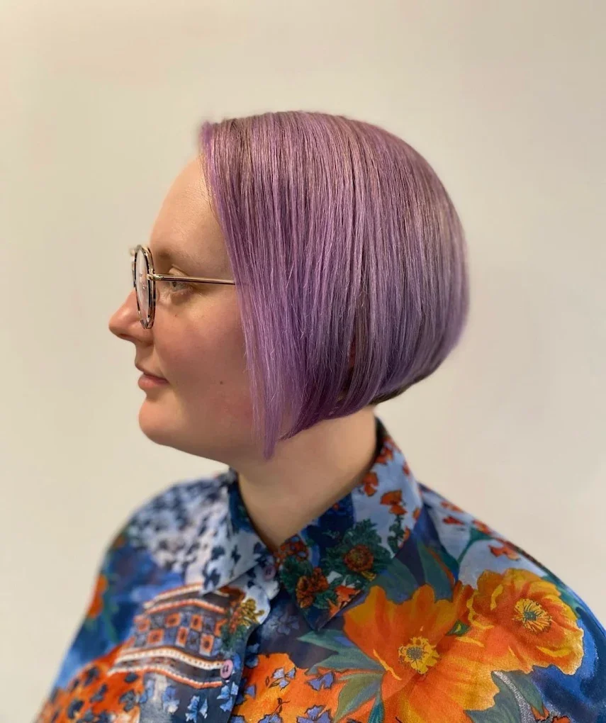Side profile of a woman with purple bob haircut, wearing round glasses and a colorful floral patterned shirt. Haircut by Tiffany Shuck of Rooted Ritual Salon, formerly Hare Salon.