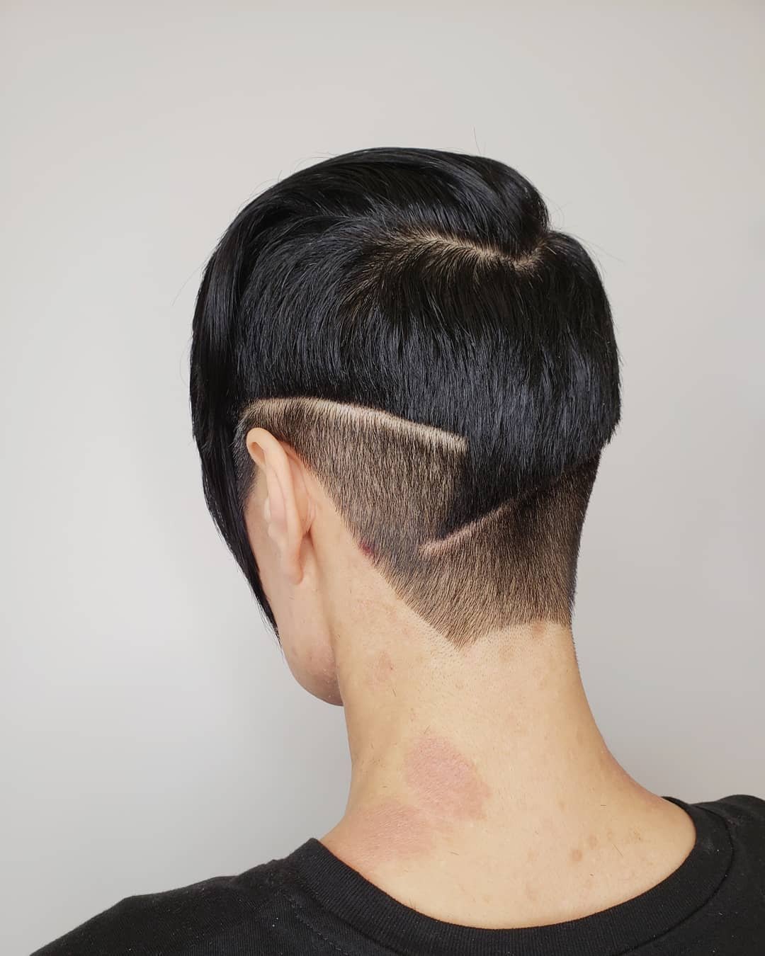 A person with a modern, asymmetric haircut featuring a shaved pattern on the side of the head. Haircut by Tiffany Shuck of Rooted Ritual Salon, formerly Hare Salon.