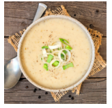Bowl of creamy soup garnished with sliced green onions on a wooden table