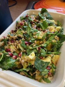 A bowl of fresh salad with chopped greens, pomegranate seeds, avocado, and other vegetables.