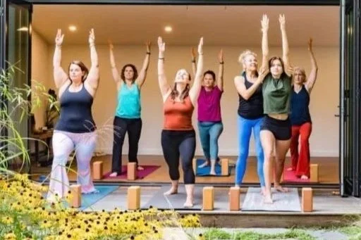 A group of women participating in an outdoor yoga session at sunrise, practicing yoga poses on mats.