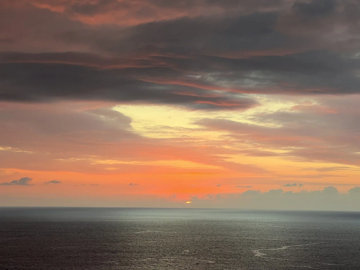 Sunset over the ocean with colorful clouds in the sky.