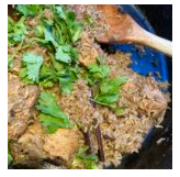 Fried chicken pieces in a black skillet with green herbs on top.