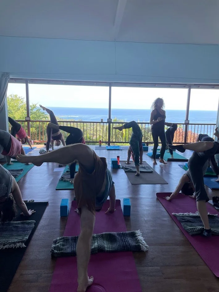 Group of people practicing yoga in a studio with large windows and ocean view.