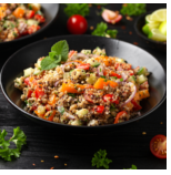 Close-up of a bowl of cooked quinoa salad with cherry tomatoes, chopped vegetables, herbs, and seasoning.
