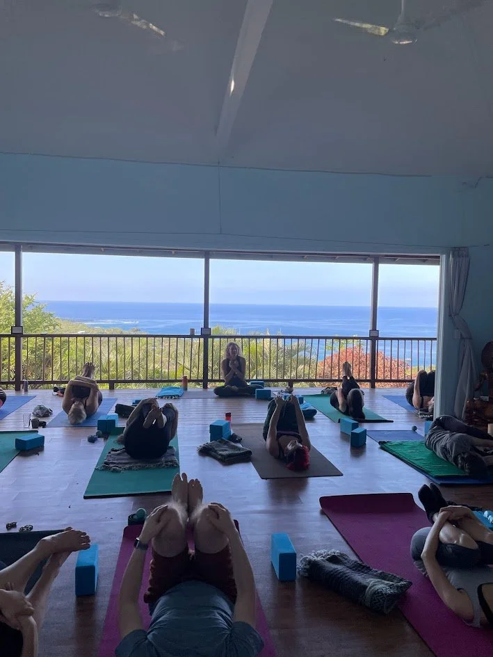 A group of people practicing yoga in a room with a large window overlooking the ocean.