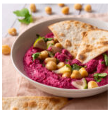 A bowl of beet hummus topped with chickpeas and parsley, served with pita bread.