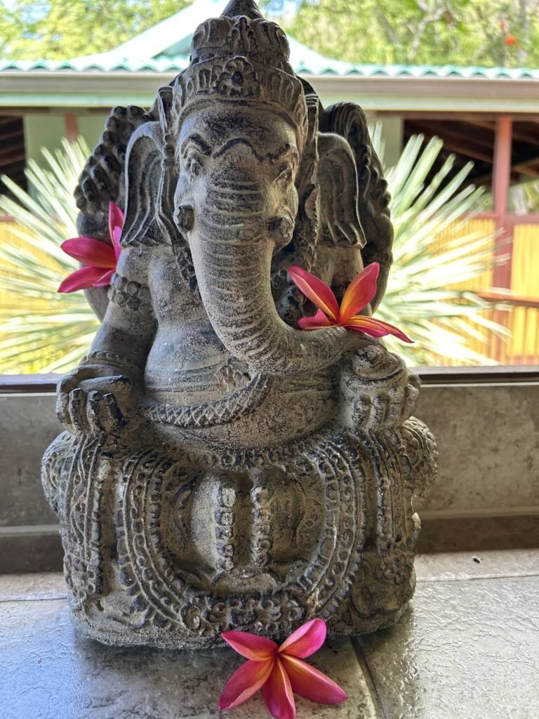 Stone statue of the Hindu deity Ganesha with pink flowers around it.