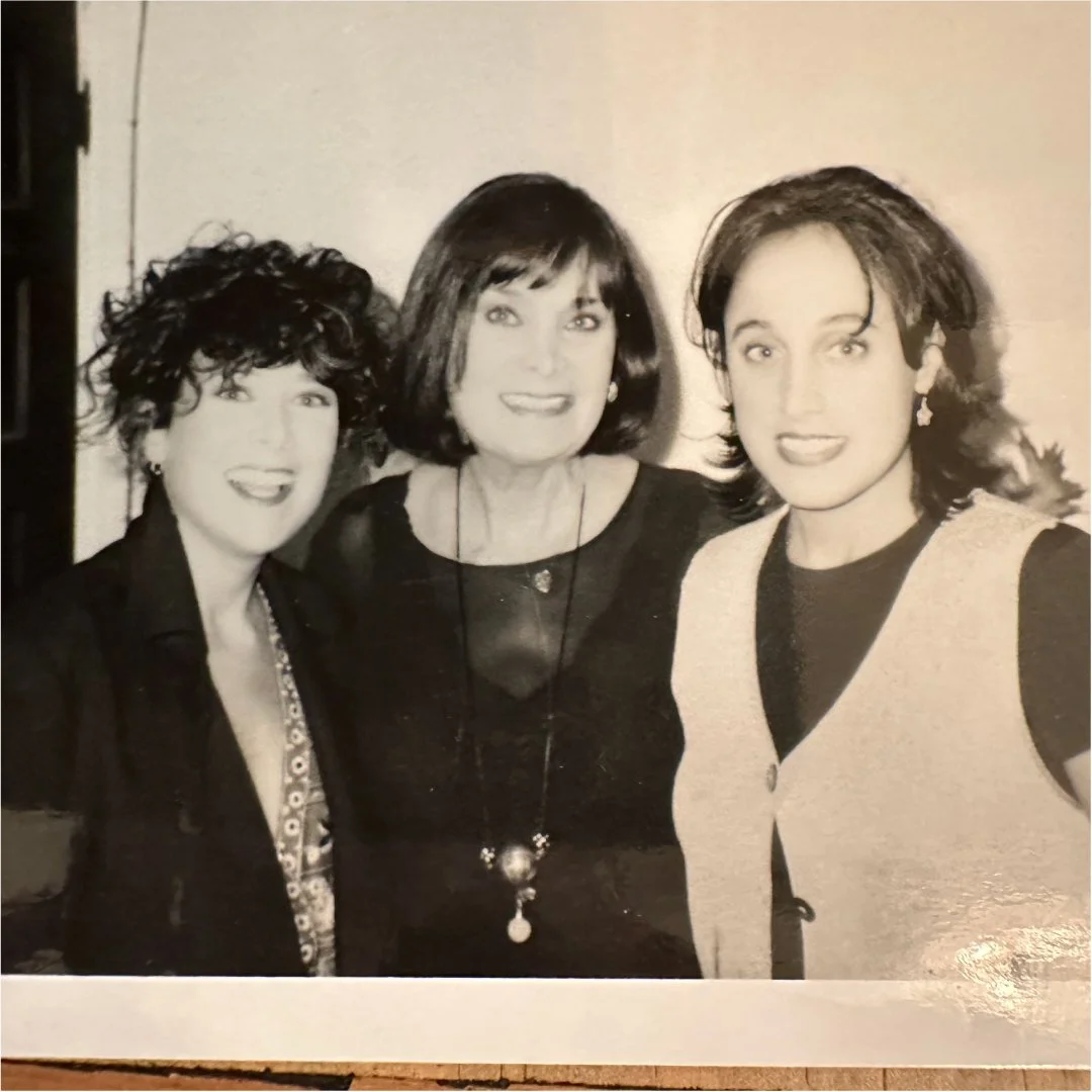 Black and white photo of three women smiling and posing together, dressed in stylish clothing.